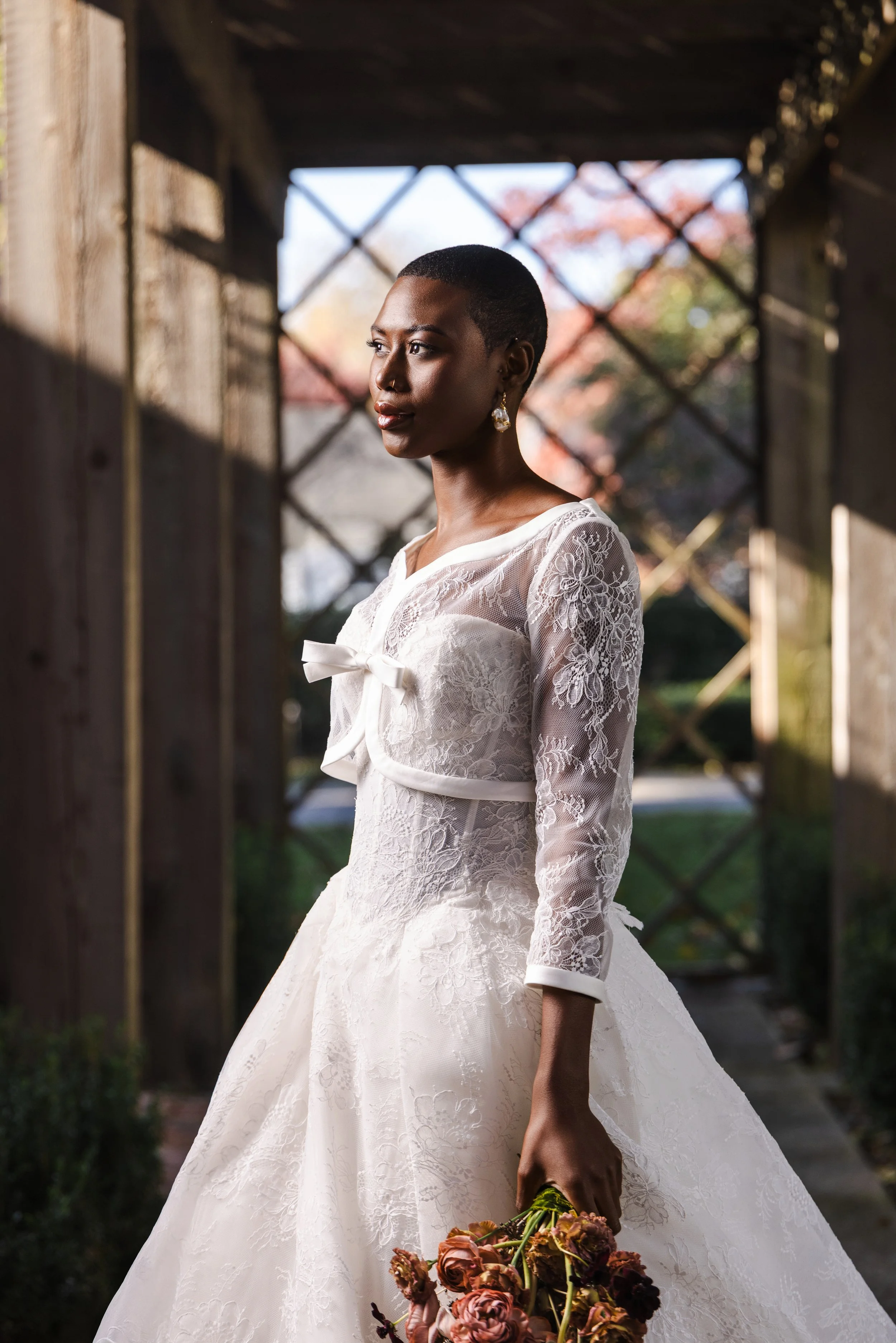 Close-up of bride in sheer lace jacket and bow detail, softly lit by sunrise through the wooden beams at the Watson House