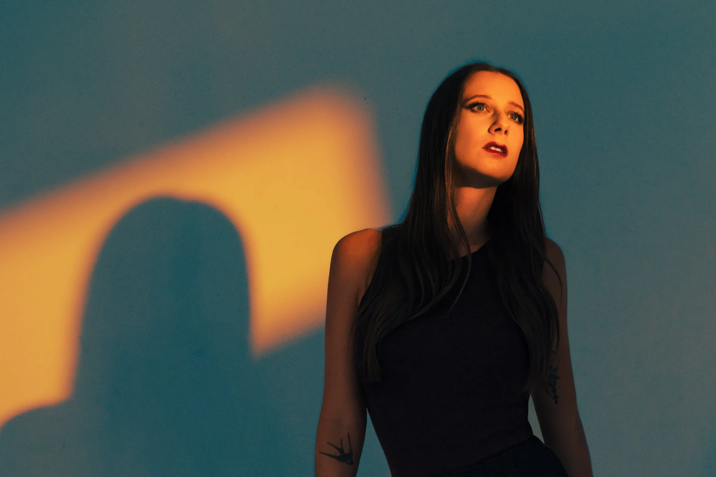 Dramatic studio portrait of Lauren River lit with a narrow snoot slice and blue gel fill, creating bold contrast and cinematic shadows in a two-light lighting setup.