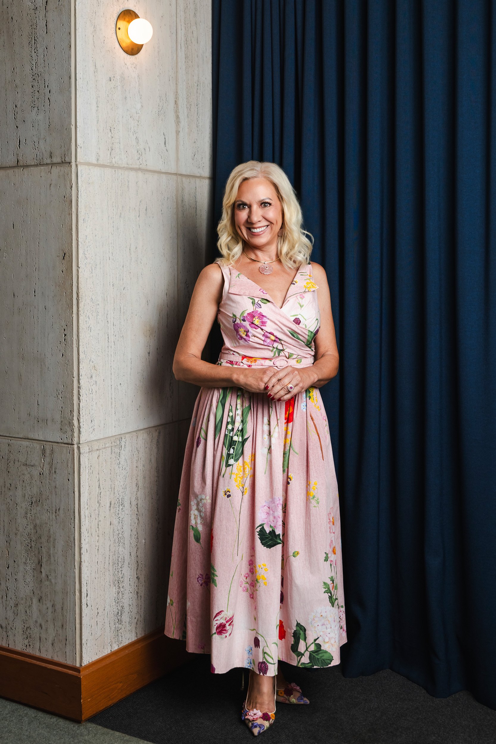 Julia Baker in a blush floral wrap dress against the travertine wall and navy curtain at the Fairlane Hotel, Nashville.