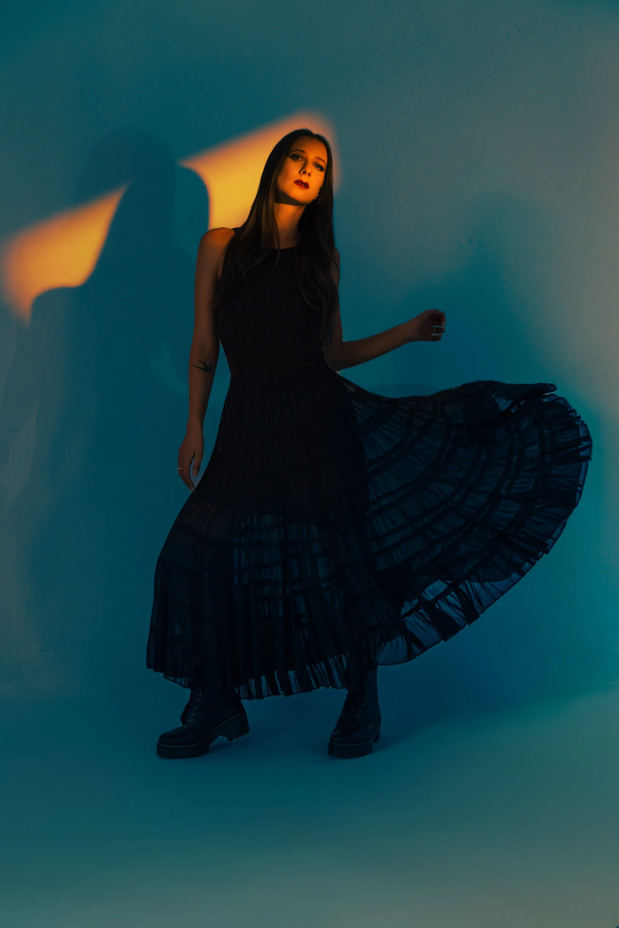 Full-body artist portrait of Lauren River with a narrow snoot slice of orange gel light and blue fill creating dramatic contrast in a two-light studio lighting setup.