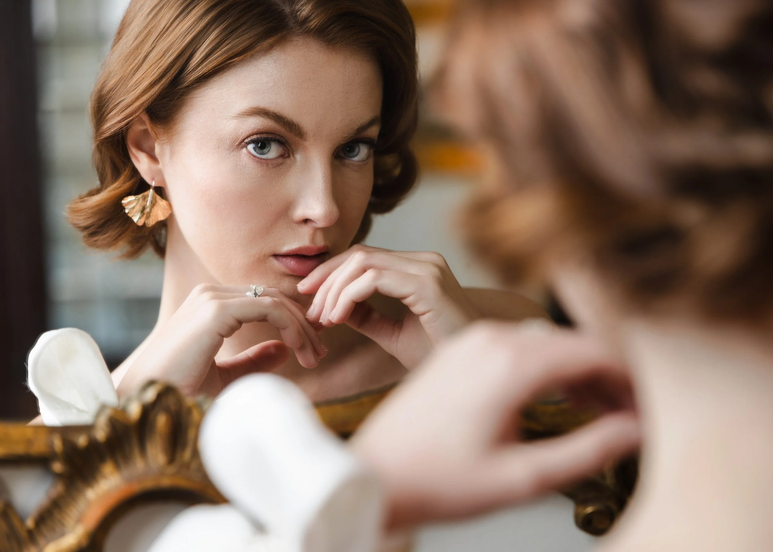 Close-up of bride with vintage waves and sculptural sleeves reflected in ornate gold mirror at Watson House