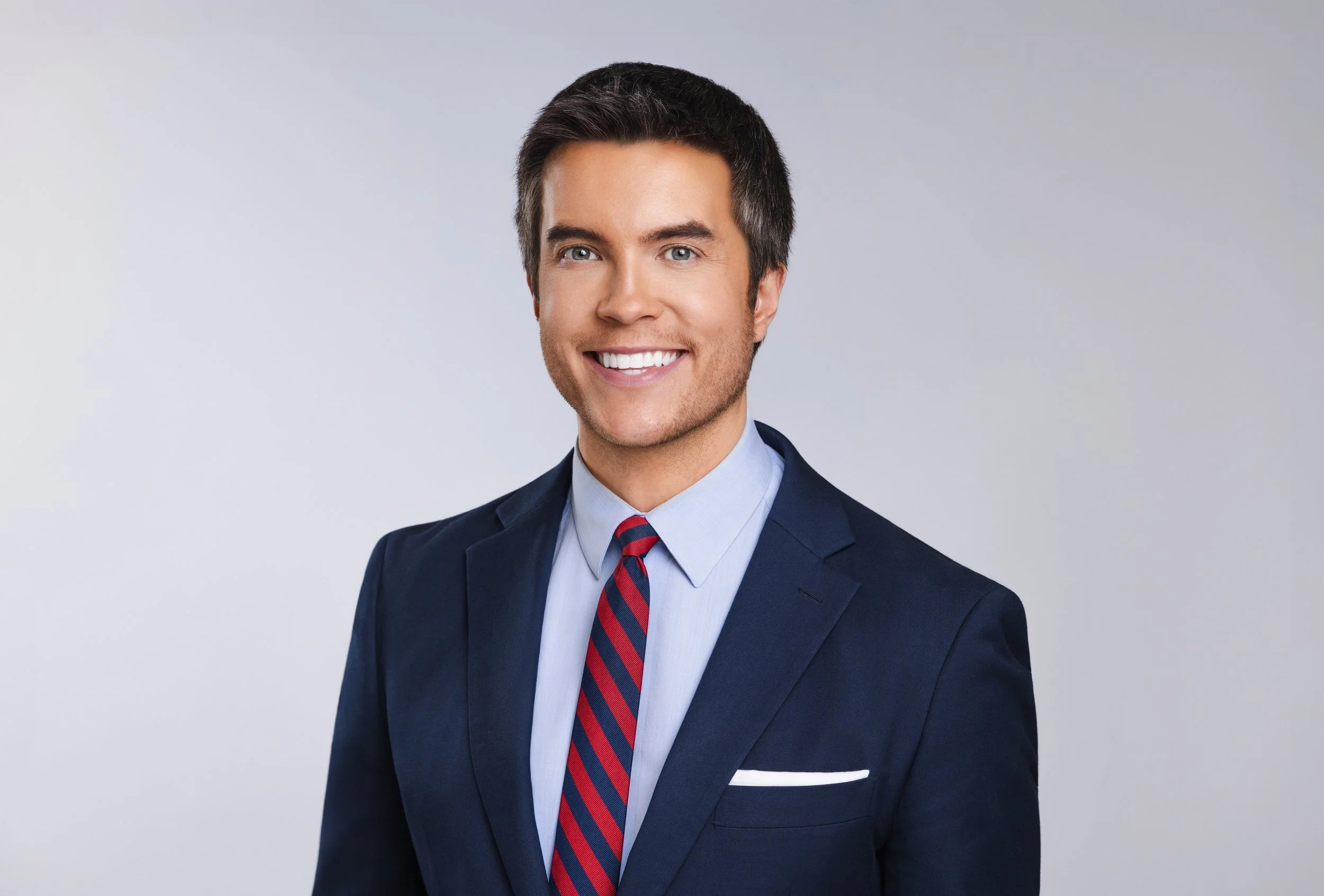 Corporate headshot of a smiling man in a navy suit with a red striped tie and pocket square.