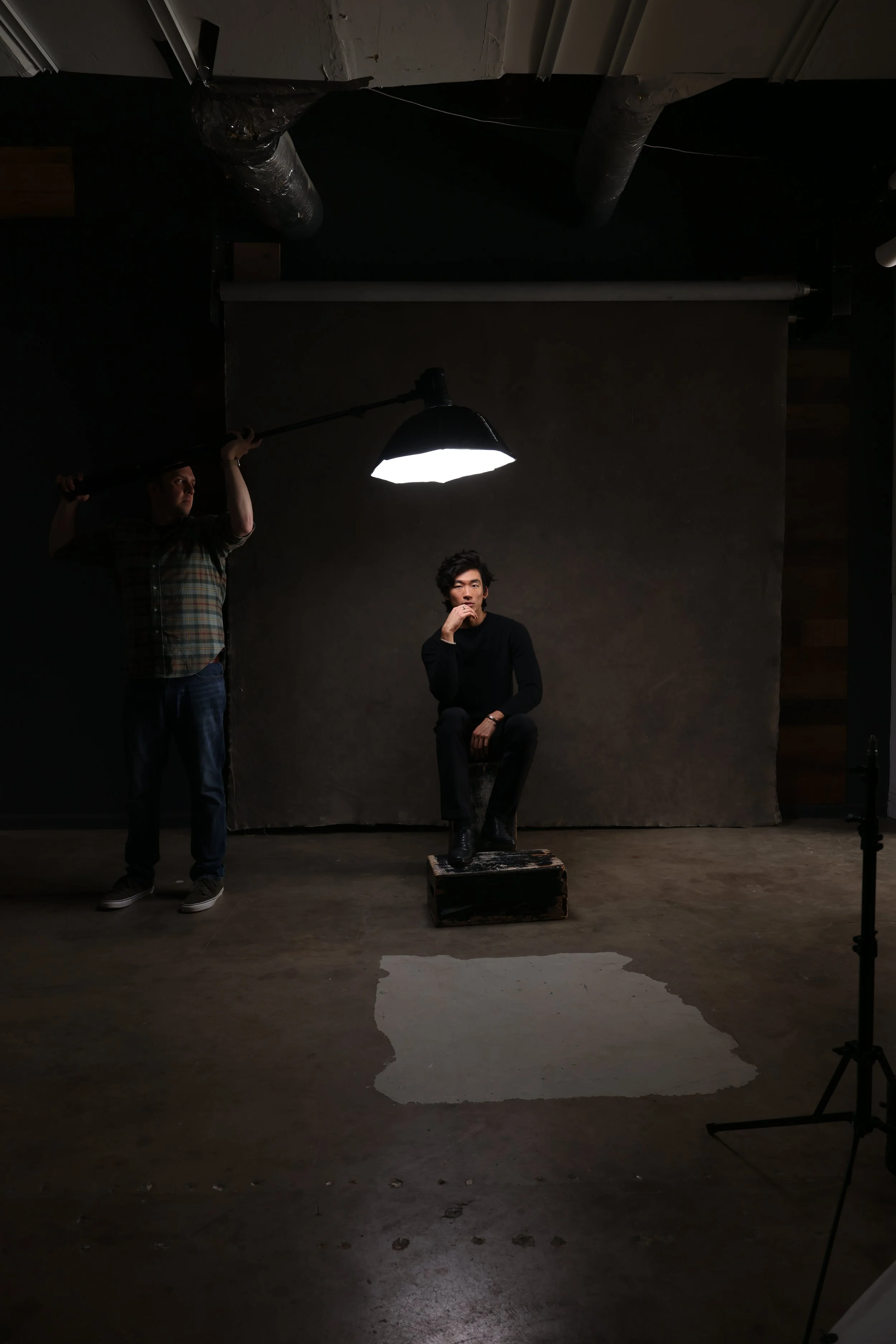 Behind the scenes photo of Nashville portrait photography session showing boom light setup with seated male subject against grey backdrop