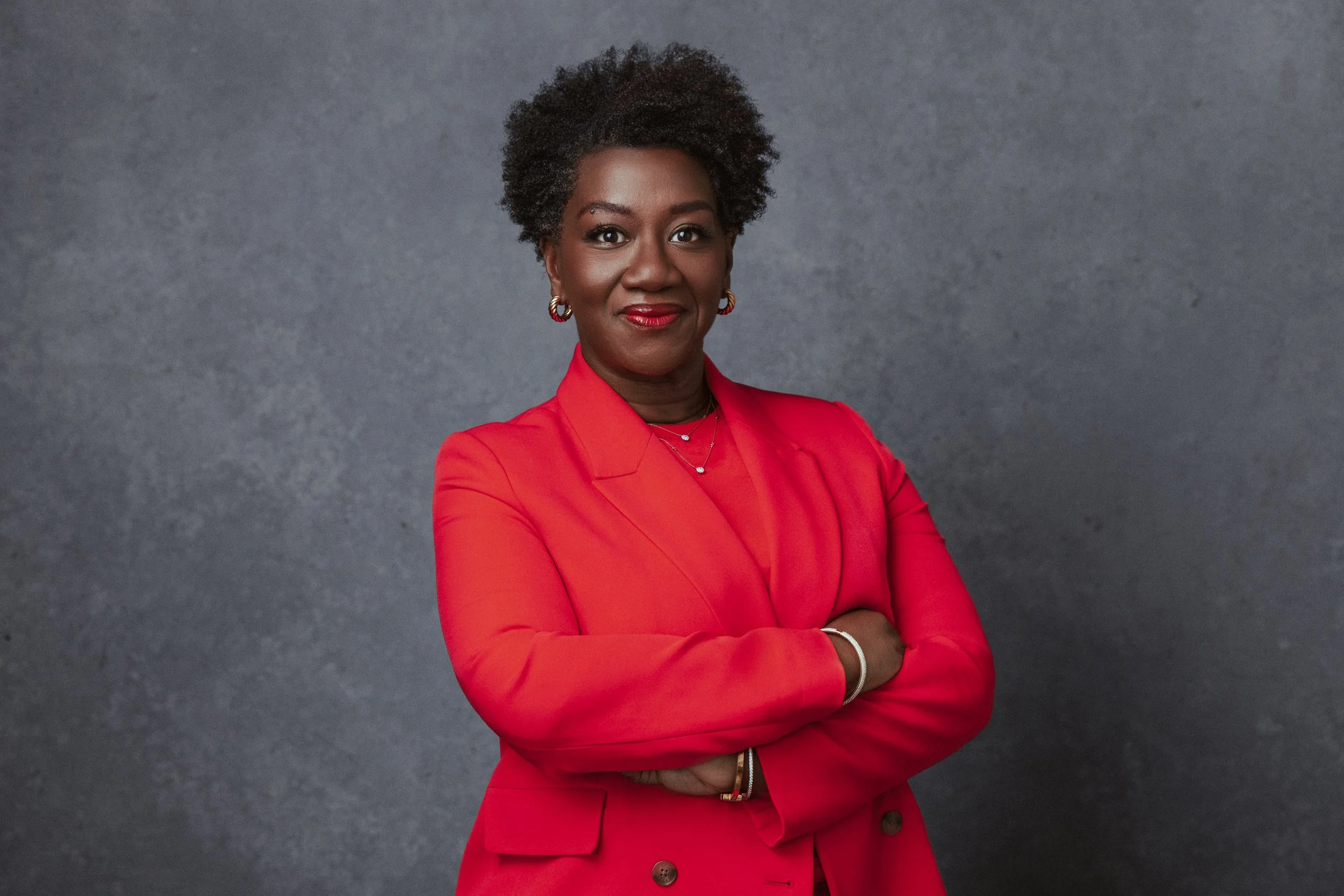 A bold, confident portrait of Tressie McMillan Cottom styled in a striking red suit. This professional image, captured by a Nashville Commercial Photographer, uses a neutral backdrop and direct pose to reflect authority and leadership—ideal for brand