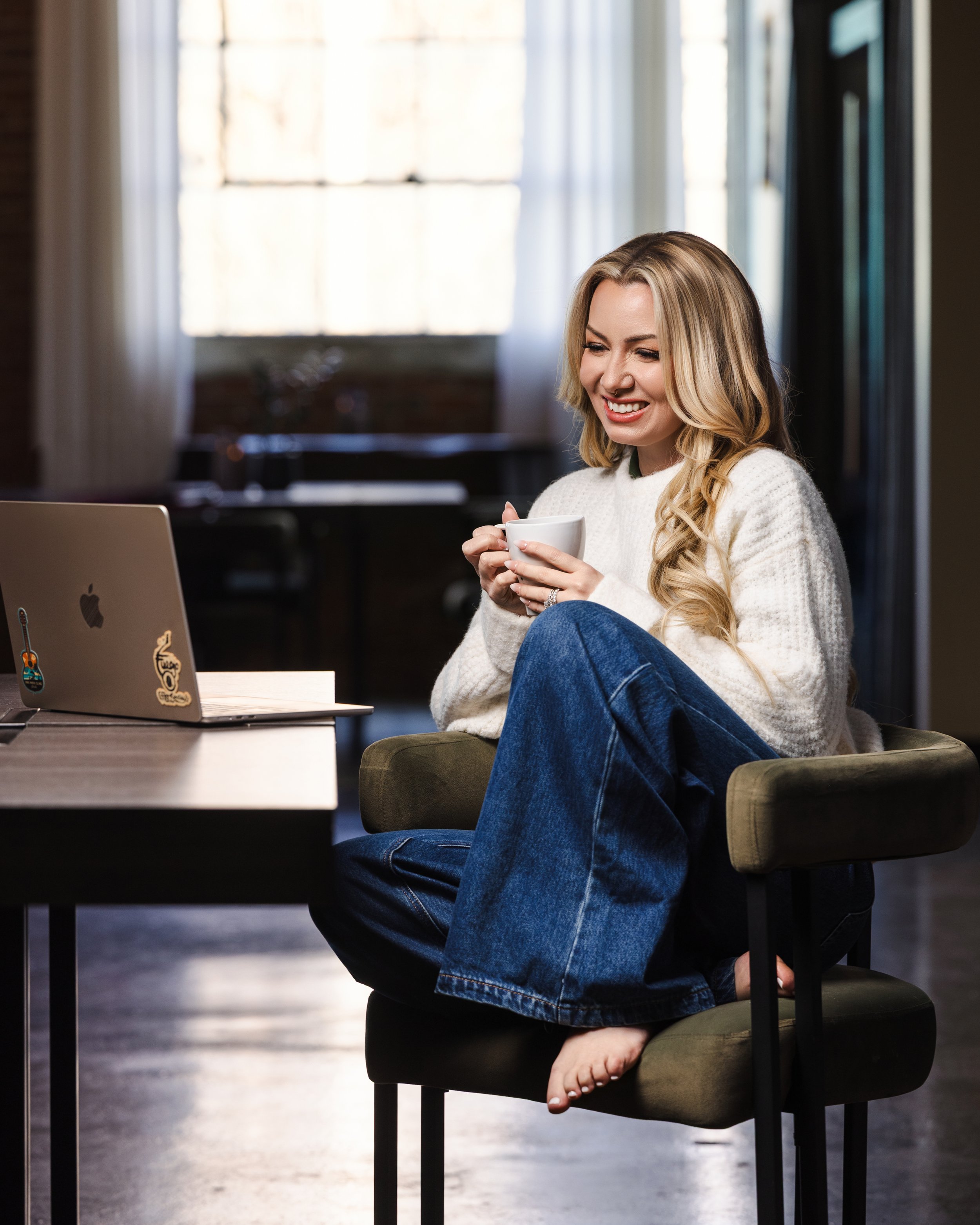 Personal branding portrait of a female entrepreneur sitting with a laptop and coffee, representing visibility, leadership, and business growth.