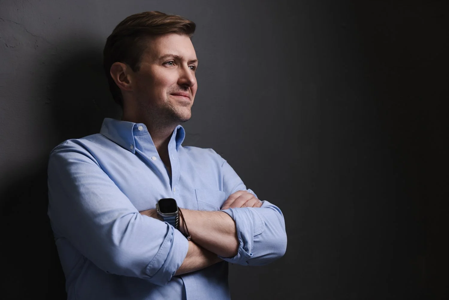 Studio headshot of a man in a light blue shirt with arms crossed against a dark background, photographed by Tausha Dickinson Photography in Nashville