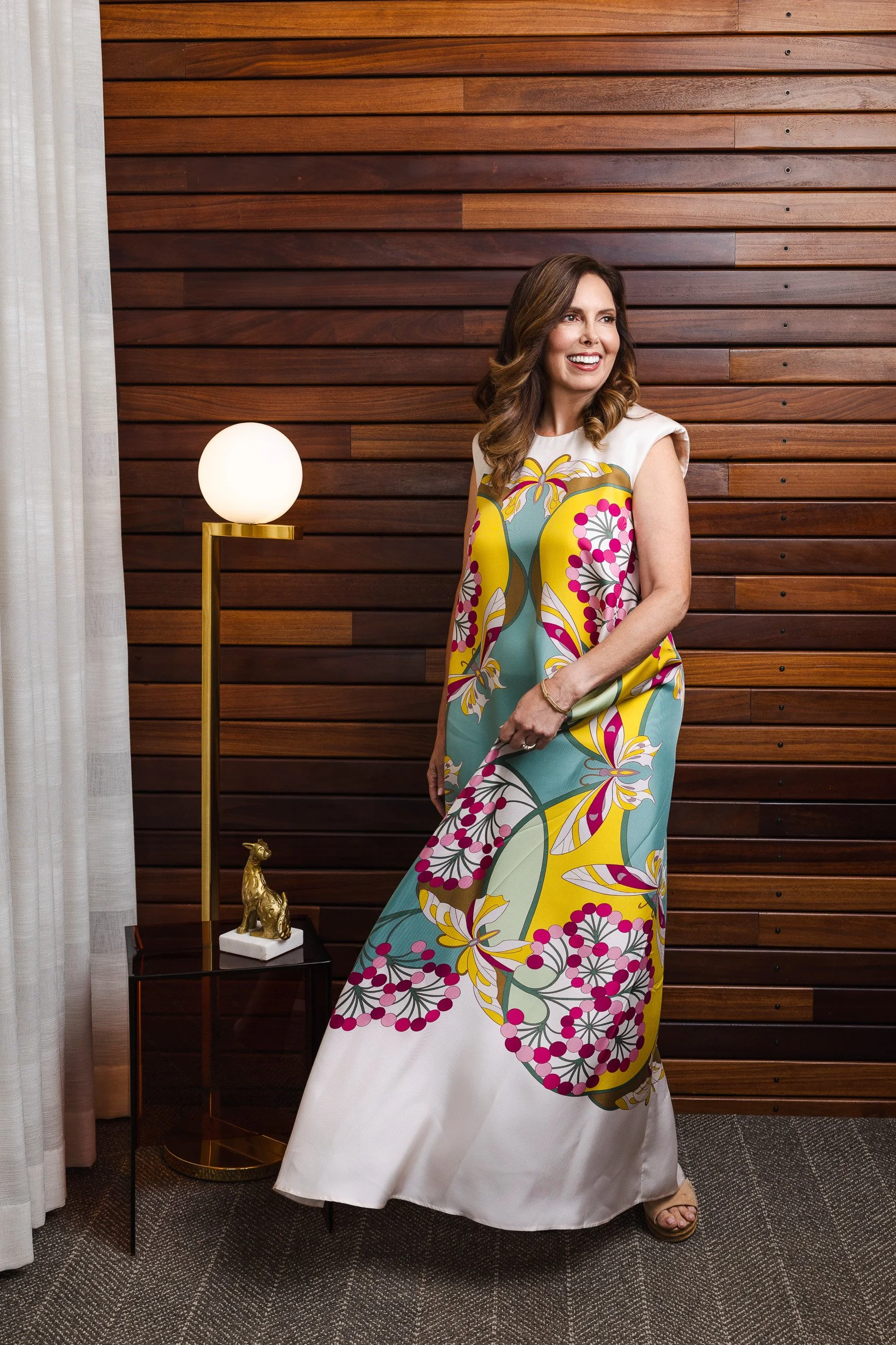 Renee Bates in a colorful maximalist print dress, photographed against a dark wood slat wall for her Nashville editorial portrait.
