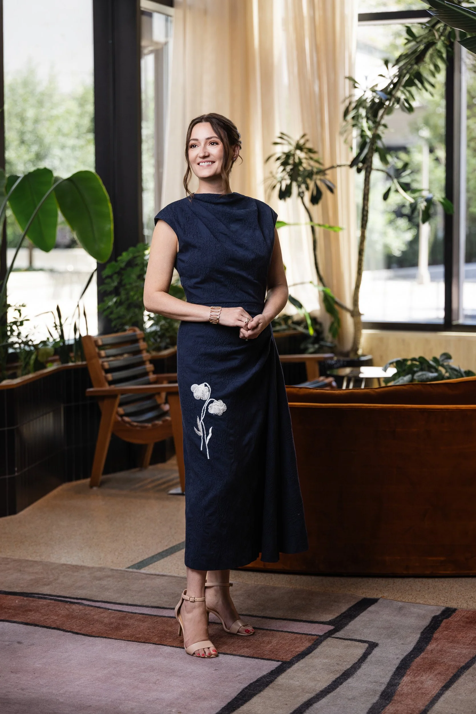 Alice Hudson Pell in a navy floral dress during her Model Behavior 2026 editorial portrait session in Nashville, surrounded by lush greenery and a rust velvet lounge chair.