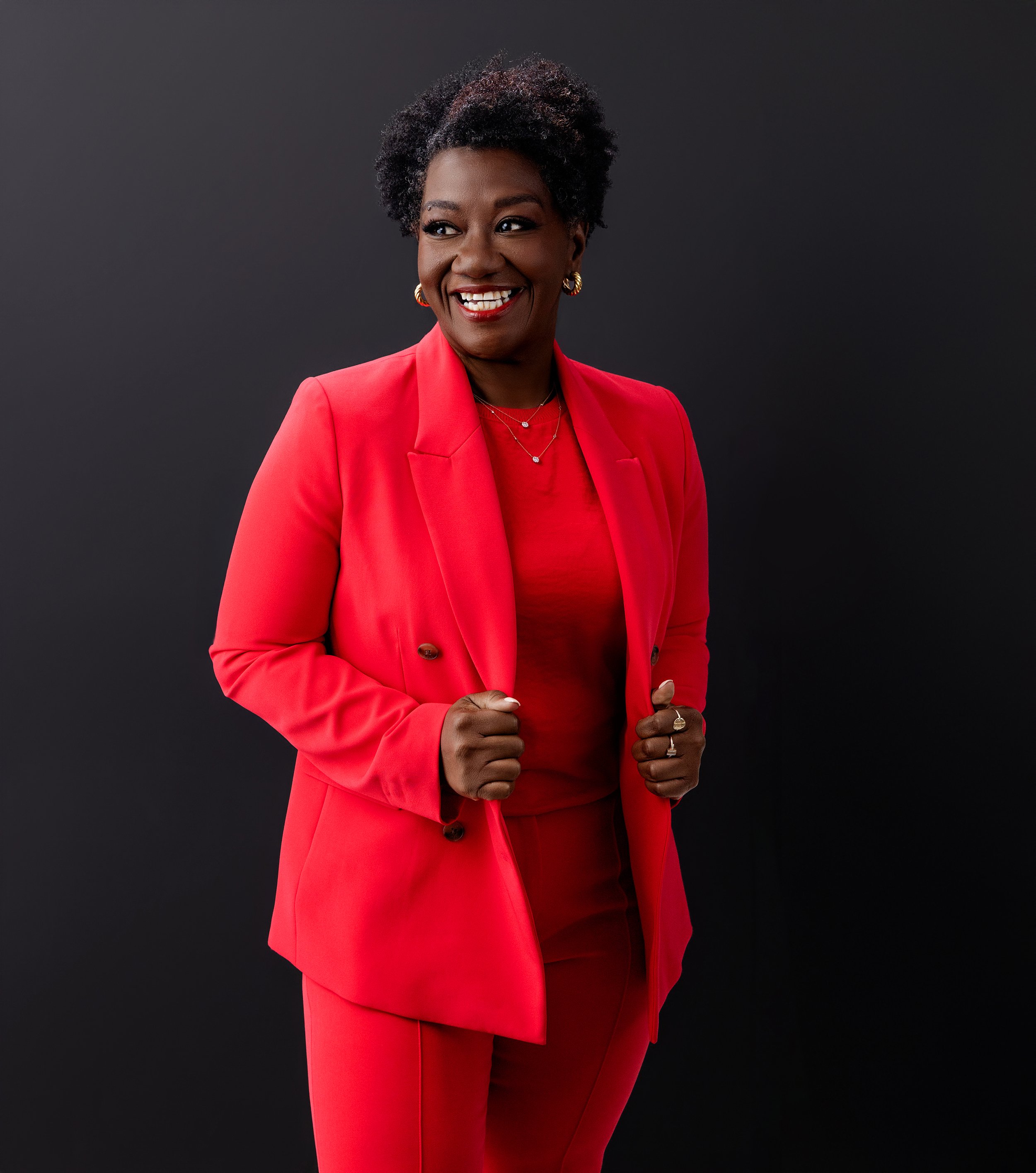 Bold and dynamic portrait of Tressie McMillan Cottom in a striking red suit against a dark background. This image radiates energy, leadership, and unapologetic style.