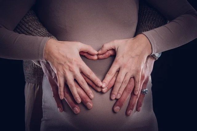 Babybauchshooting im Studio – Hände der Eltern formen ein Herz auf dem Bauch