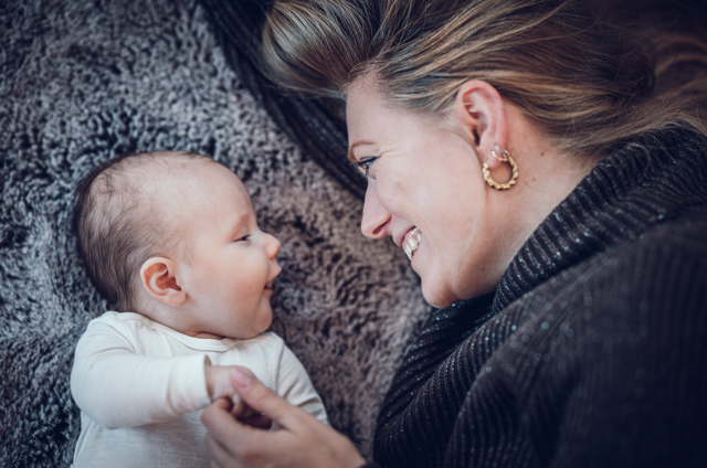 Newbornfotografie – Mutter liegt mit ihrem Baby auf dem Boden und schaut es liebevoll an
