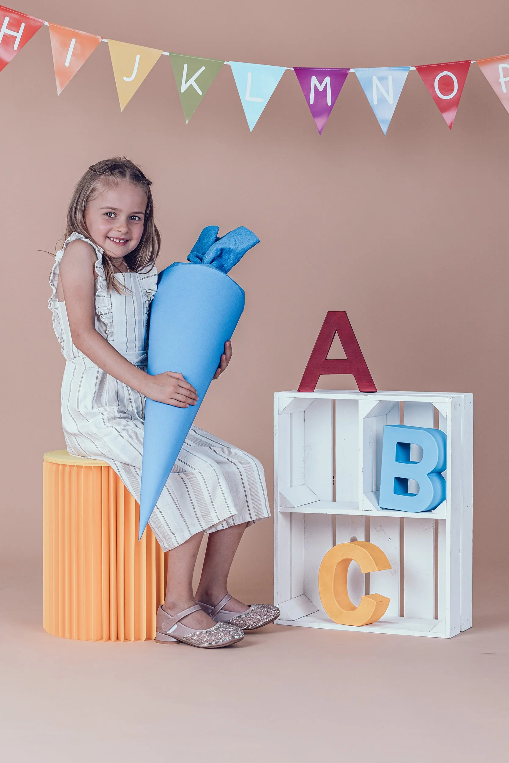 lachendes Mädchen mit großer blauer Schultüte beim Einschulungsshooting im Fotostudio in München.