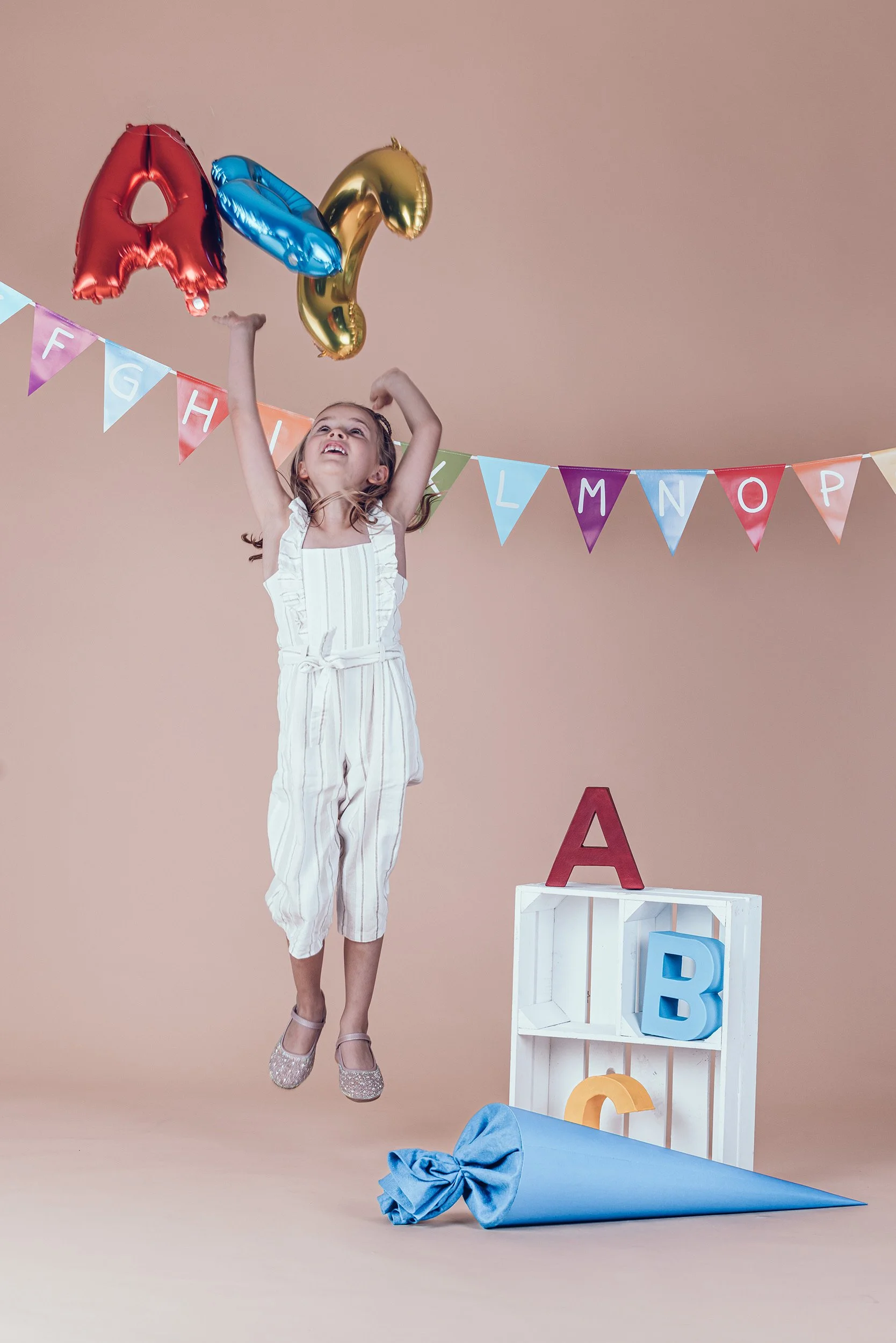 hüpfendes Mädchen mit großer blauer Schultüte beim Einschulungsshooting im Fotostudio in München.