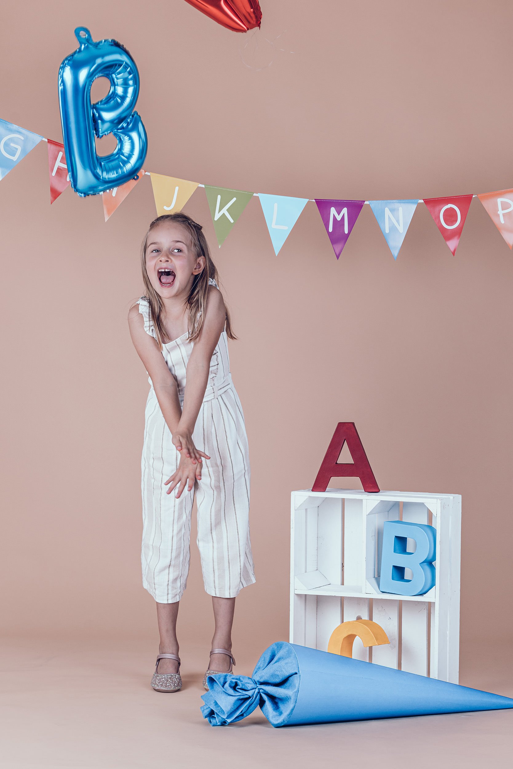 lachendes Mädchen mit großer blauer Schultüte beim Einschulungsshooting im Fotostudio in München.