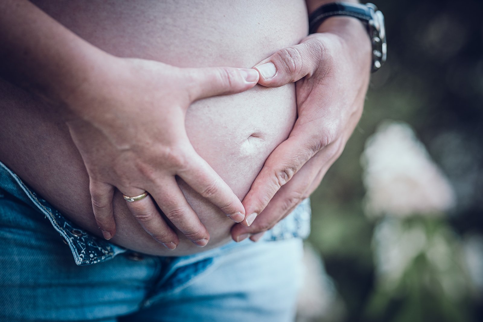 Babybauch Fotografie in der Natur – Hände halten den runden Bauch, natürliche Schwangerschaftsfotografie in München