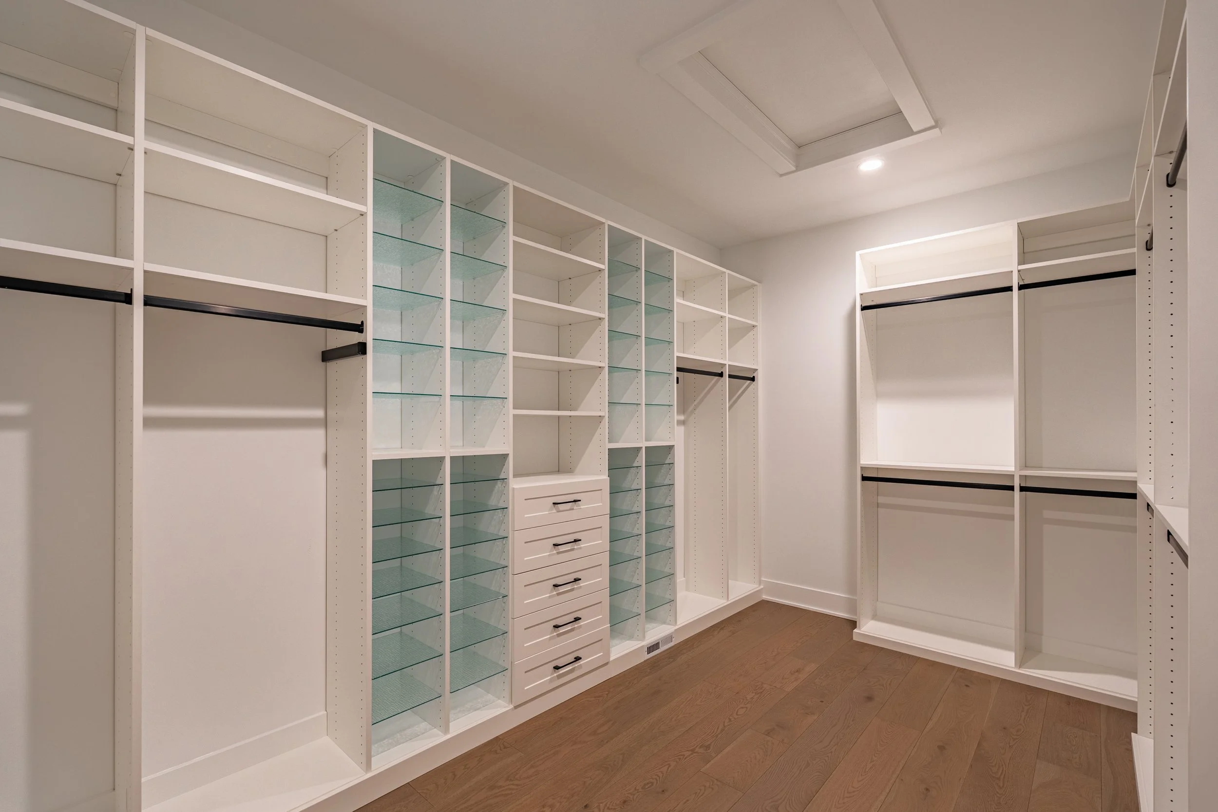 Empty white walk-in closet with shelves, drawers, and hanging rods.