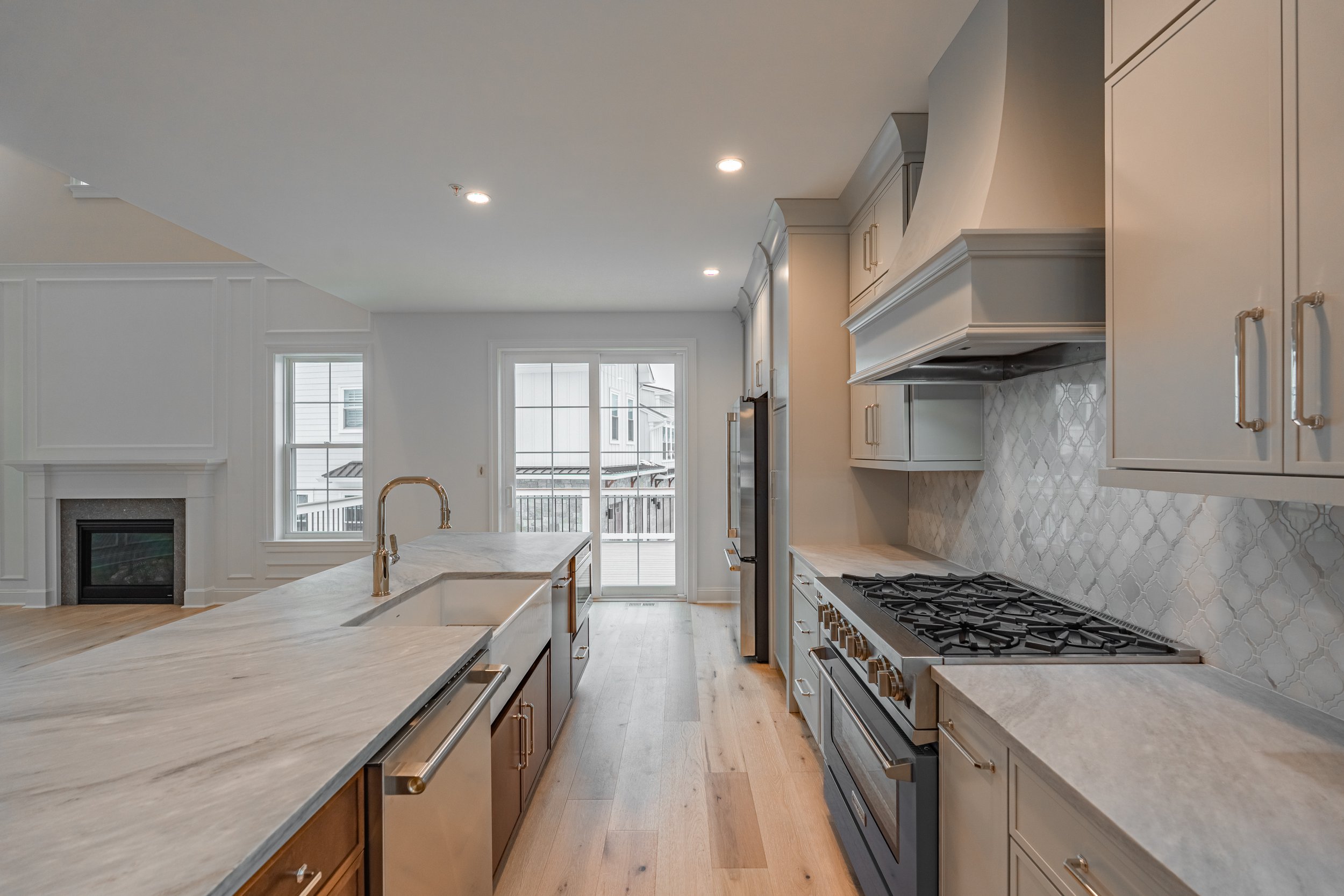 Modern kitchen with light-colored cabinets, a marble island with a sink and a gold faucet, a stainless steel stove, and large windows overlooking a balcony.