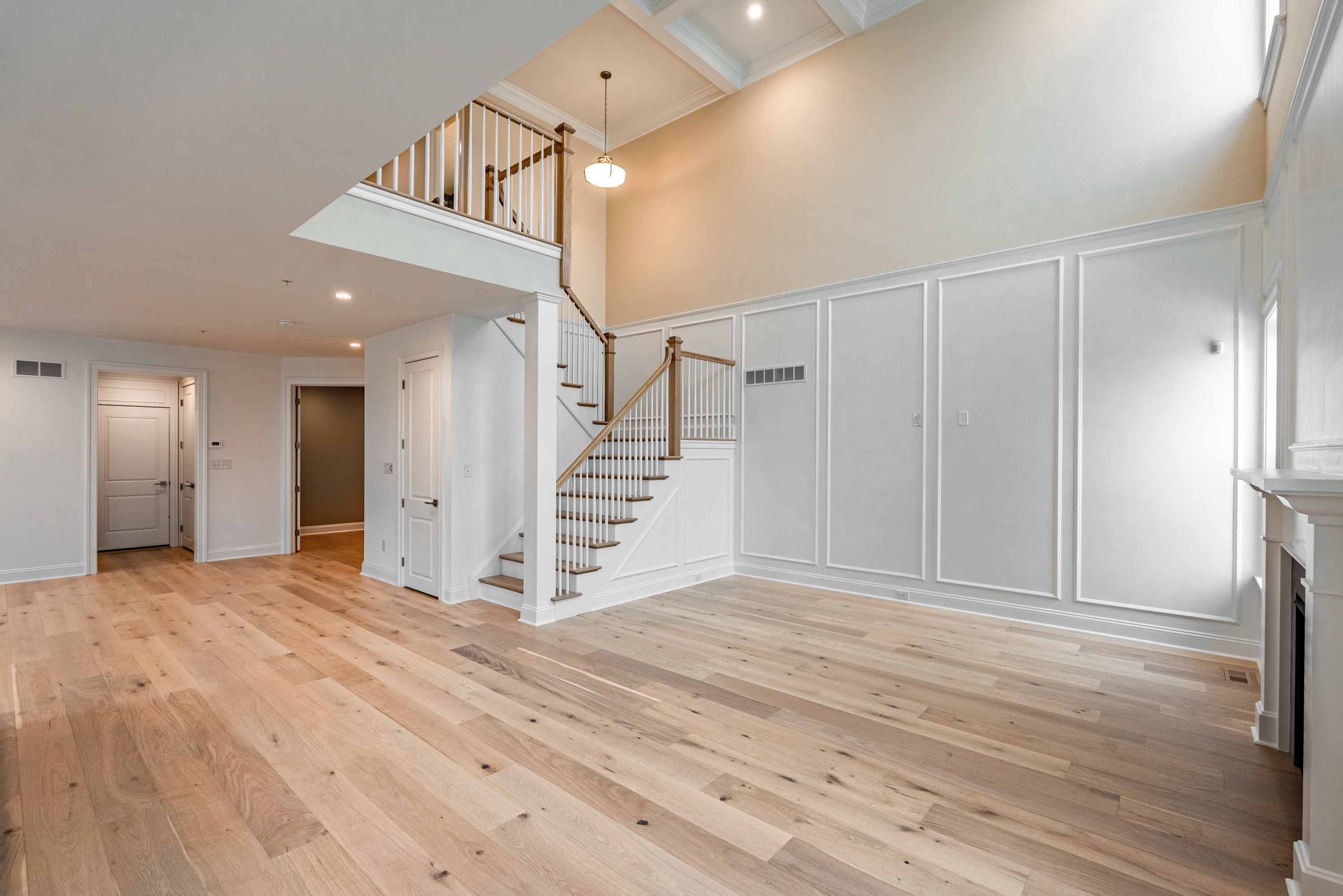 Open concept living space with hardwood floors, white walls, stairway with wooden railing, high ceiling, and skylight.