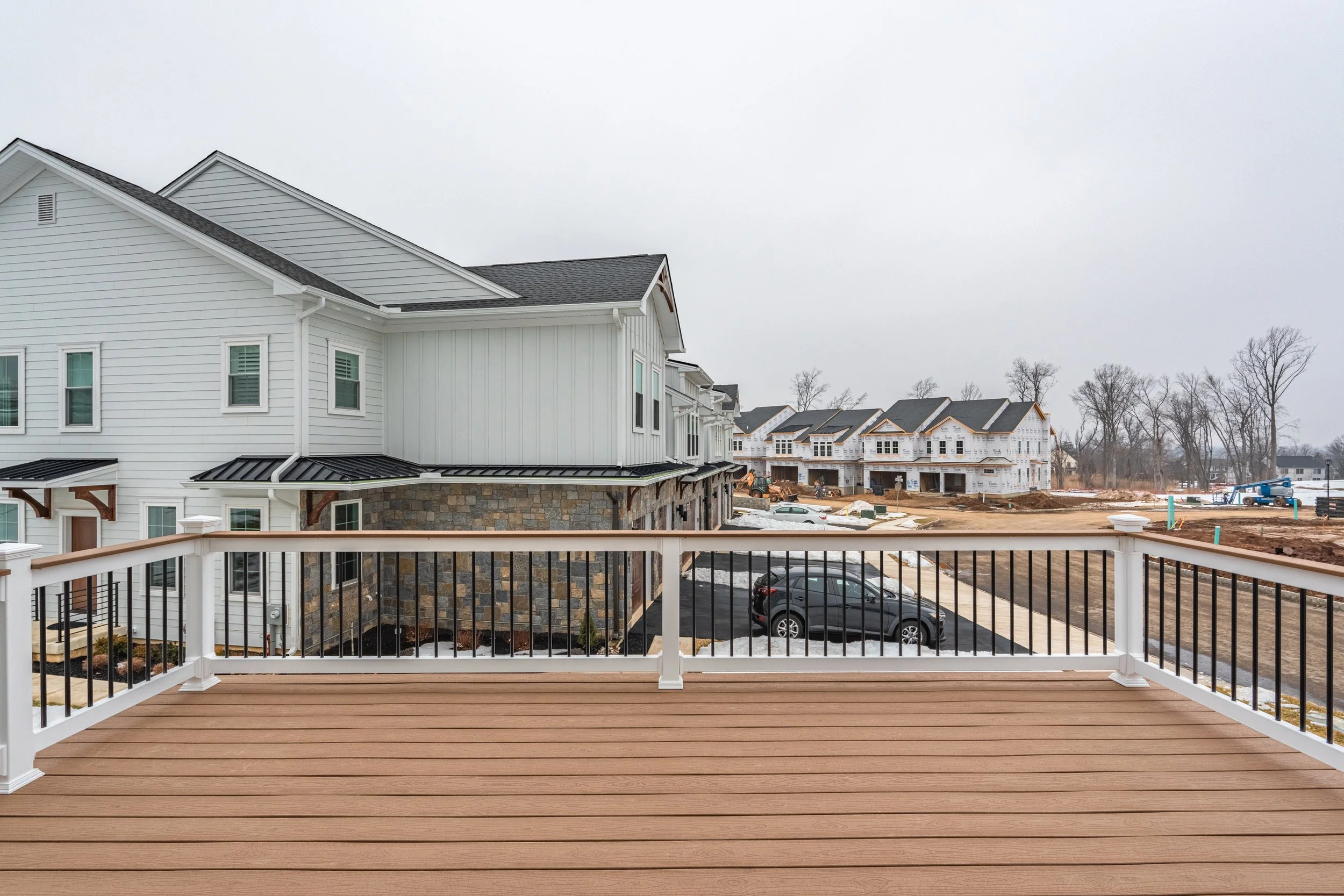 View from a balcony of a new construction residential neighborhood with houses, cars, and construction equipment on an overcast day.