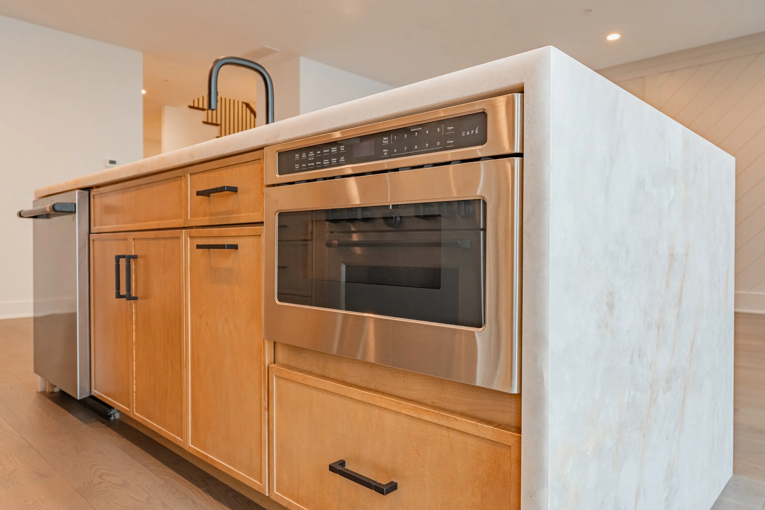 Stainless steel oven built into a wooden kitchen cabinet with a beige stone countertop and black handles in a modern kitchen.