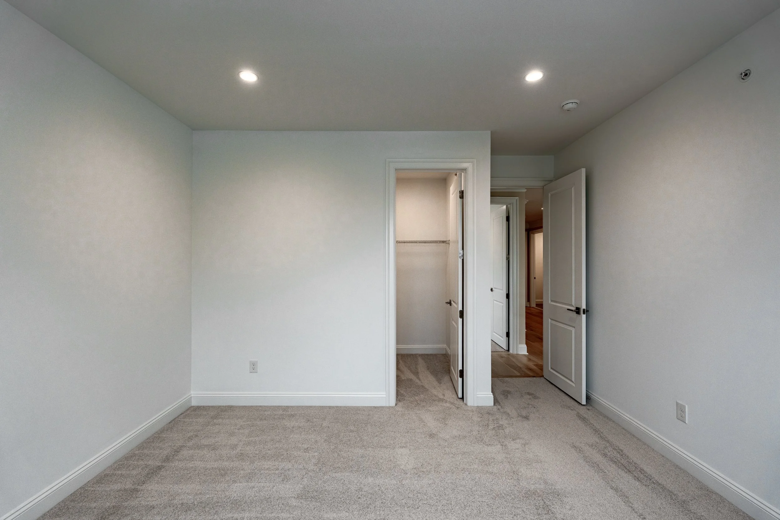 Empty room with beige carpet, white walls, and an open door leading to a closet and hallway.