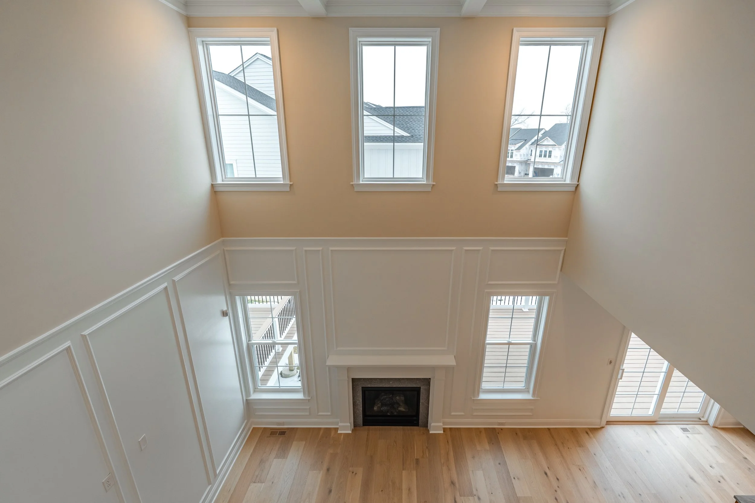 A spacious room with high ceilings, large windows letting in natural light, a fireplace, and light wooden flooring.