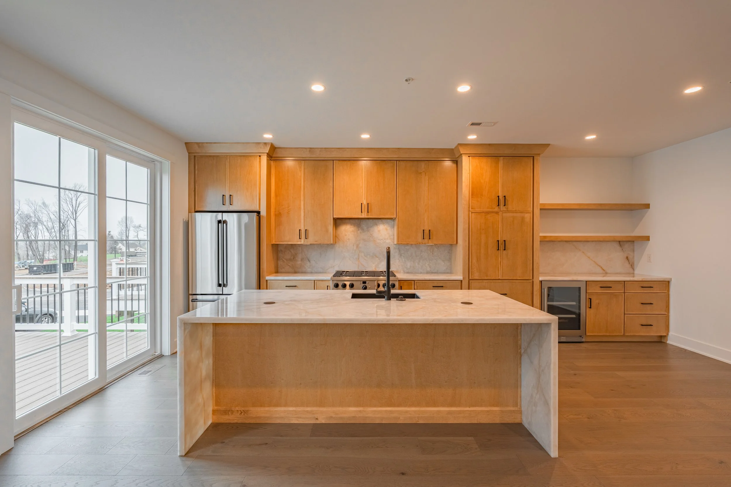 Modern kitchen with wood cabinets, marble island, stainless steel appliances, and sliding glass door leading to a patio.