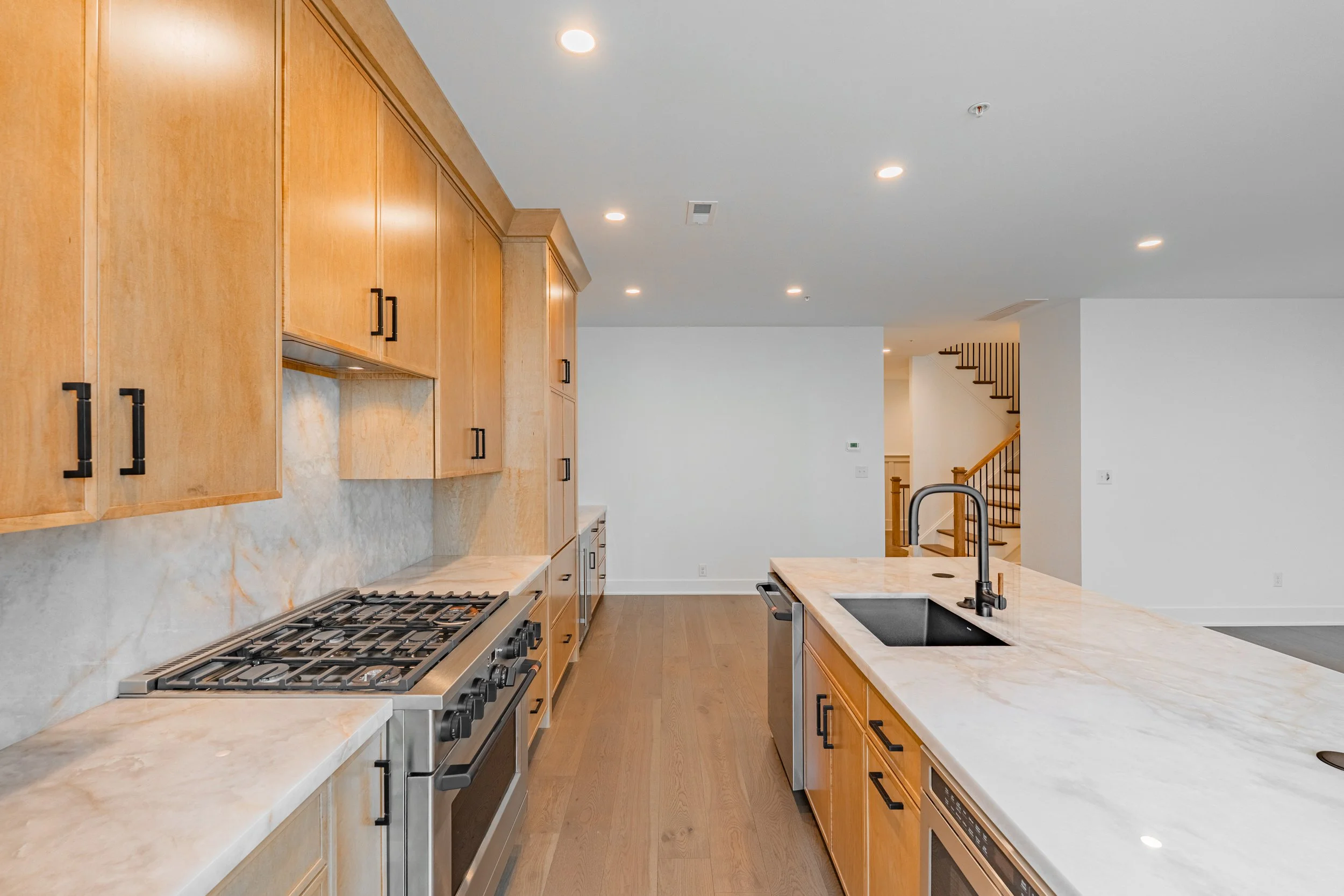 Modern kitchen with wooden cabinets, marble countertops, a gas stove, and a kitchen island with a black sink and faucet.
