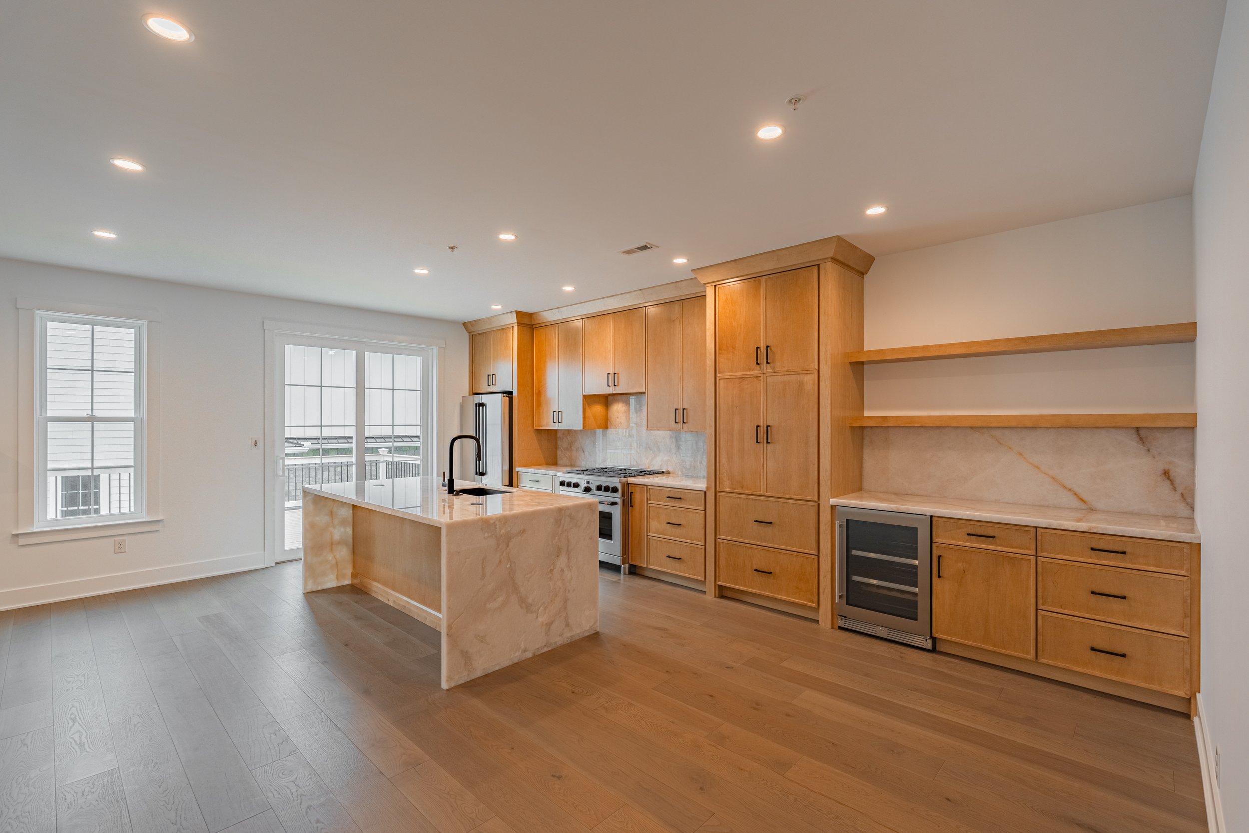Modern kitchen with wooden cabinets, marble island, stainless steel appliances, and hardwood floors.