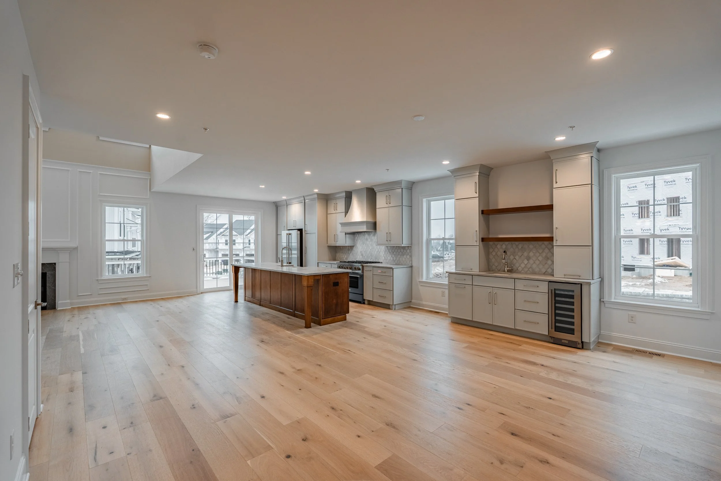 Empty modern kitchen with white cabinets, a wooden island, stainless steel appliances, and large windows, in a new home under construction.