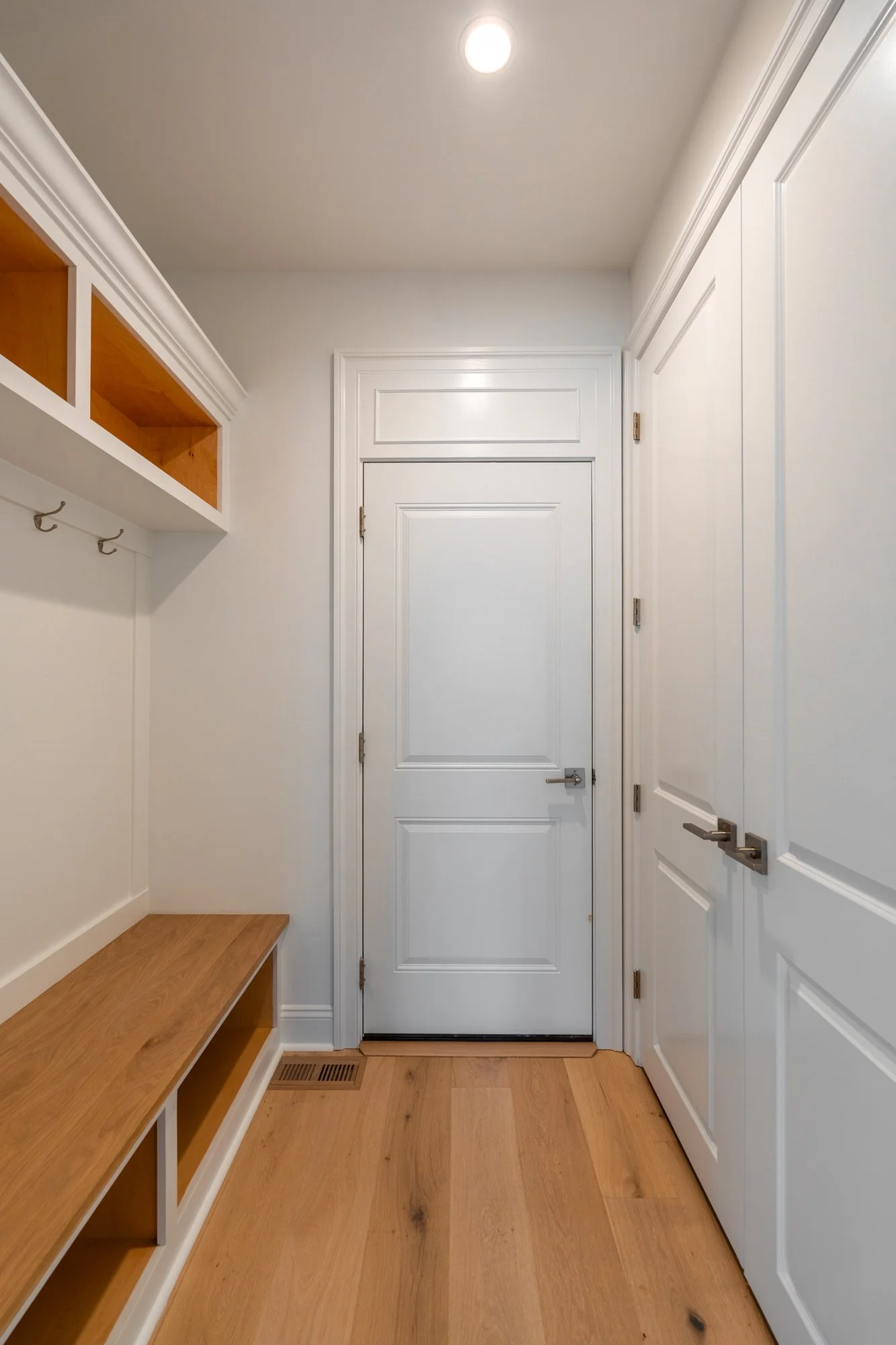 An entryway with white doors, a wooden bench, and light hardwood flooring.
