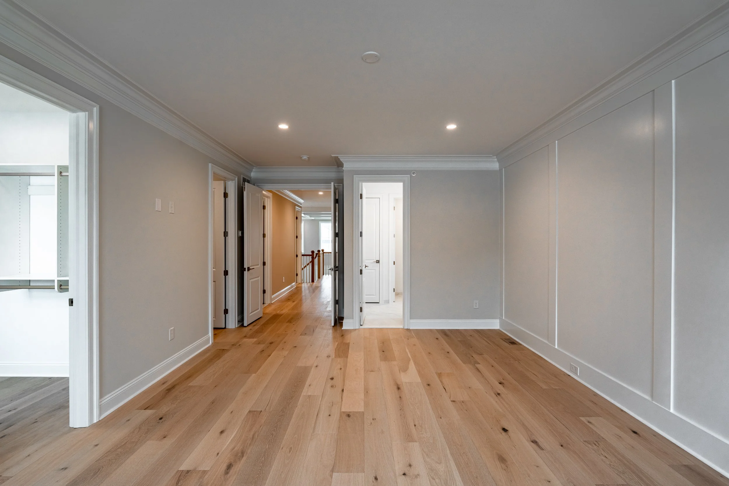 Empty room with light hardwood floors, white walls, crown molding, multiple doorways, and recessed ceiling lights.