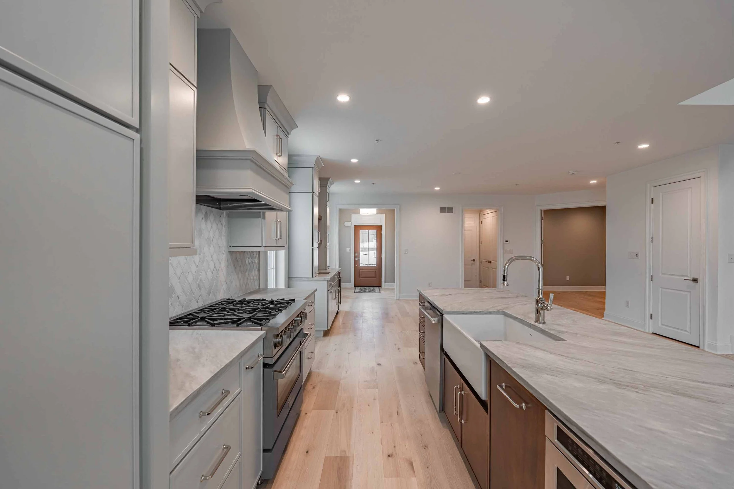 Modern kitchen with white cabinets, marble countertops, stainless steel appliances, hardwood floors, and recessed ceiling lights.
