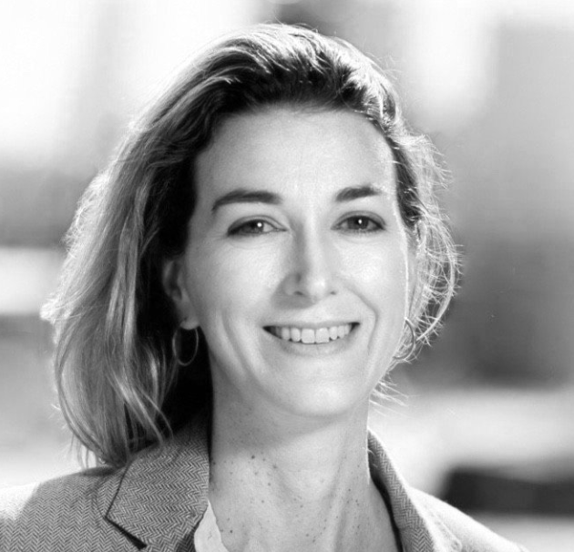 Black and white portrait of a smiling woman with shoulder-length hair, wearing a blazer and hoop earrings.