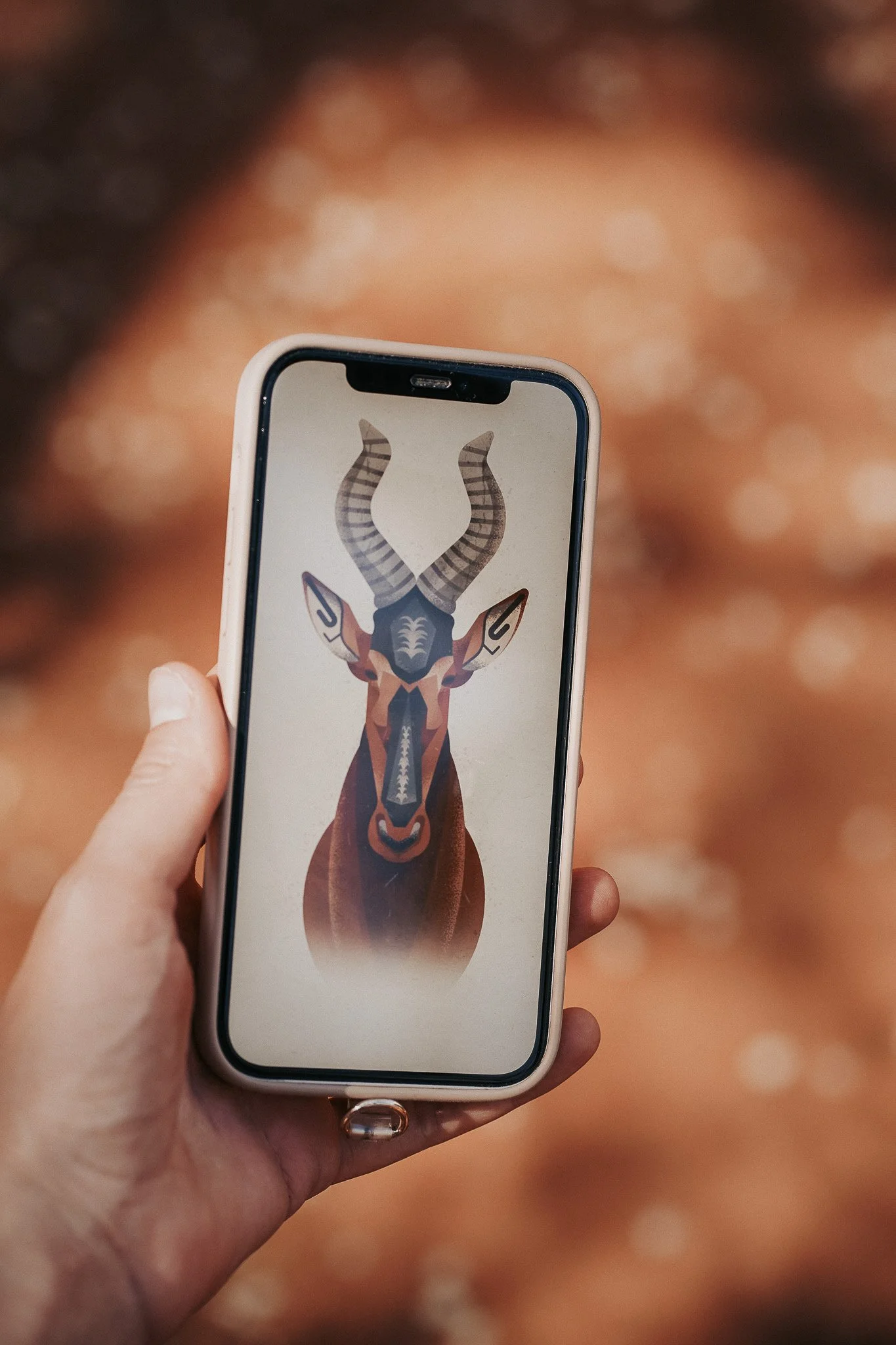 A hand holding a smartphone displaying an abstract geometric illustration of a hartebeest with patterned horns and ears.
