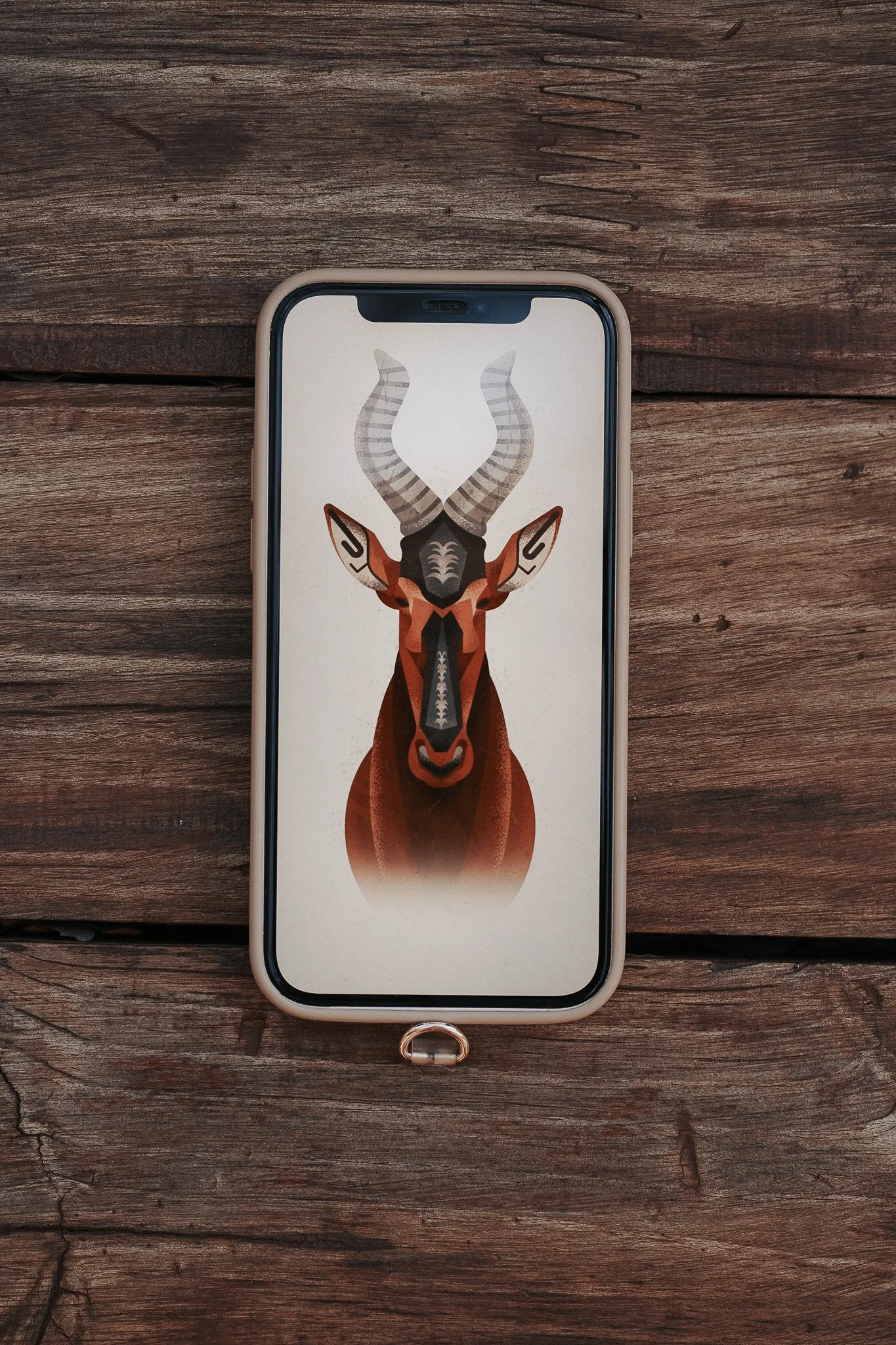 Smartphone with a geometric illustration of an hartebeests head and horns on the screen, resting on a wooden surface.