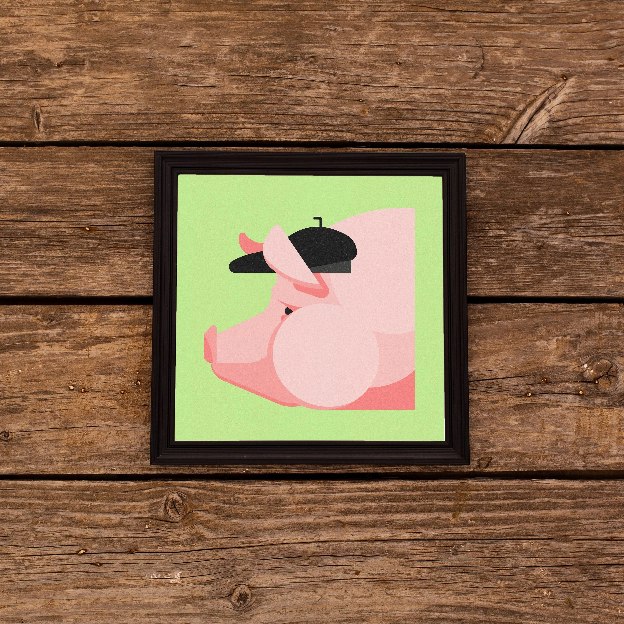A framed illustration of a pink pig with a black beret, set against a light green background, on a wooden wall.