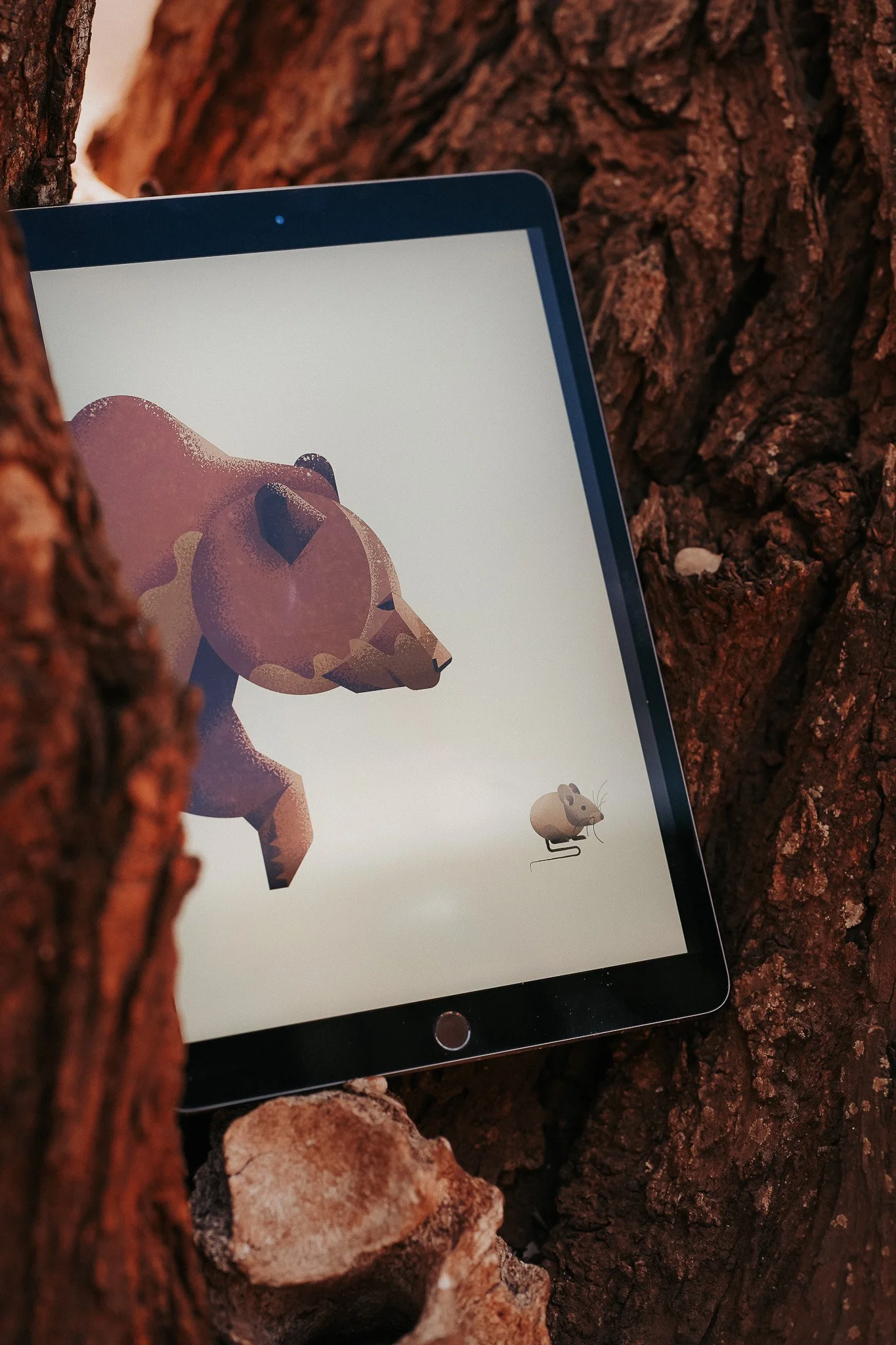 A digital illustration of a bear and a mouse on a tablet screen, set against a tree bark background.