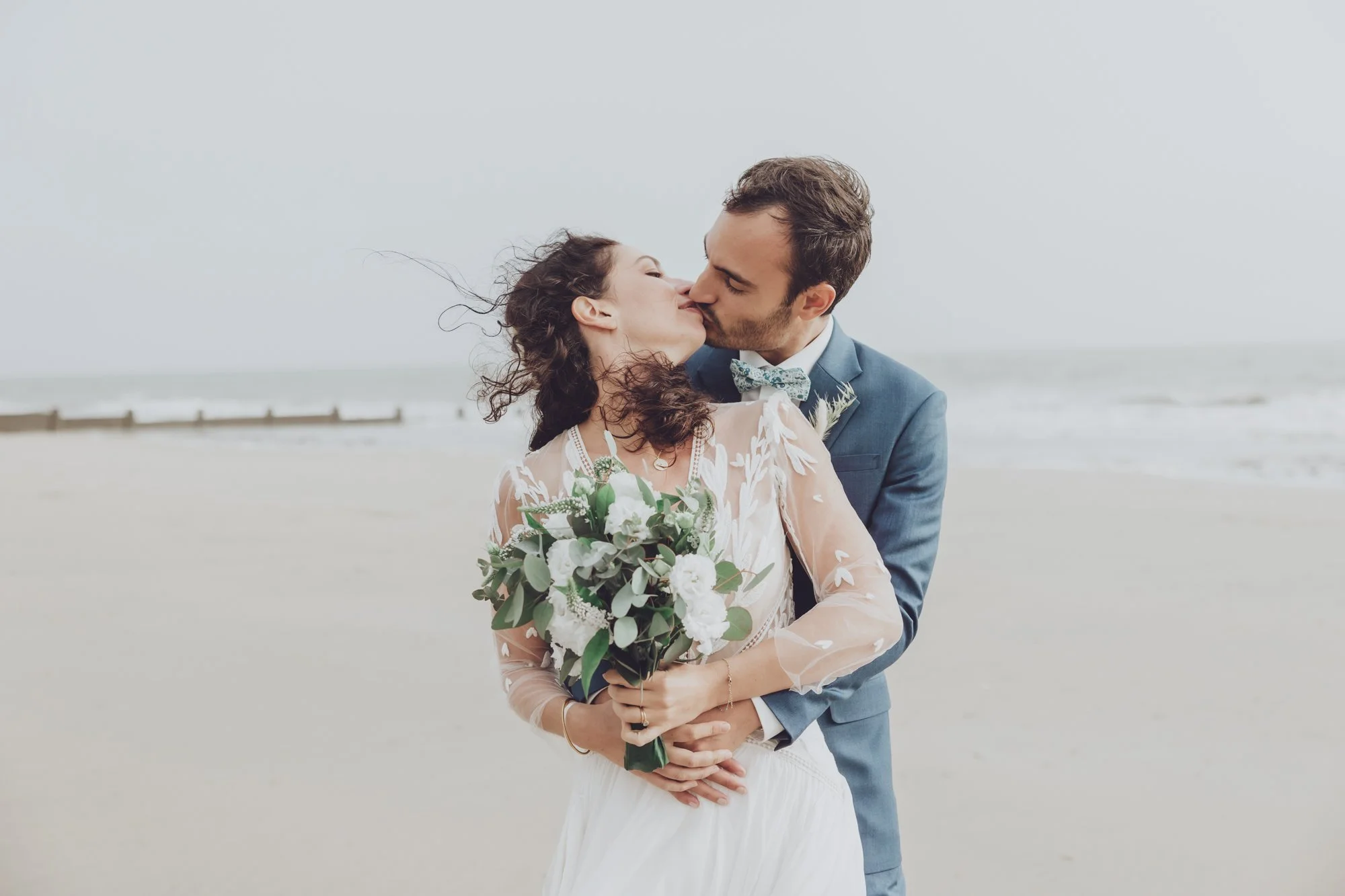 Un couple de jeunes mariés s'embrassent. Elle tient son bouquet de mariage dans les mains