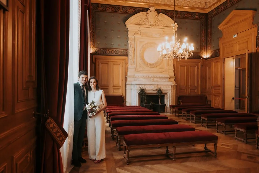 Un couple habillé pour un mariage posant à l'intérieur d'une salle élégante avec cheminée et chandelier. Par votre photographe de mariage à paris