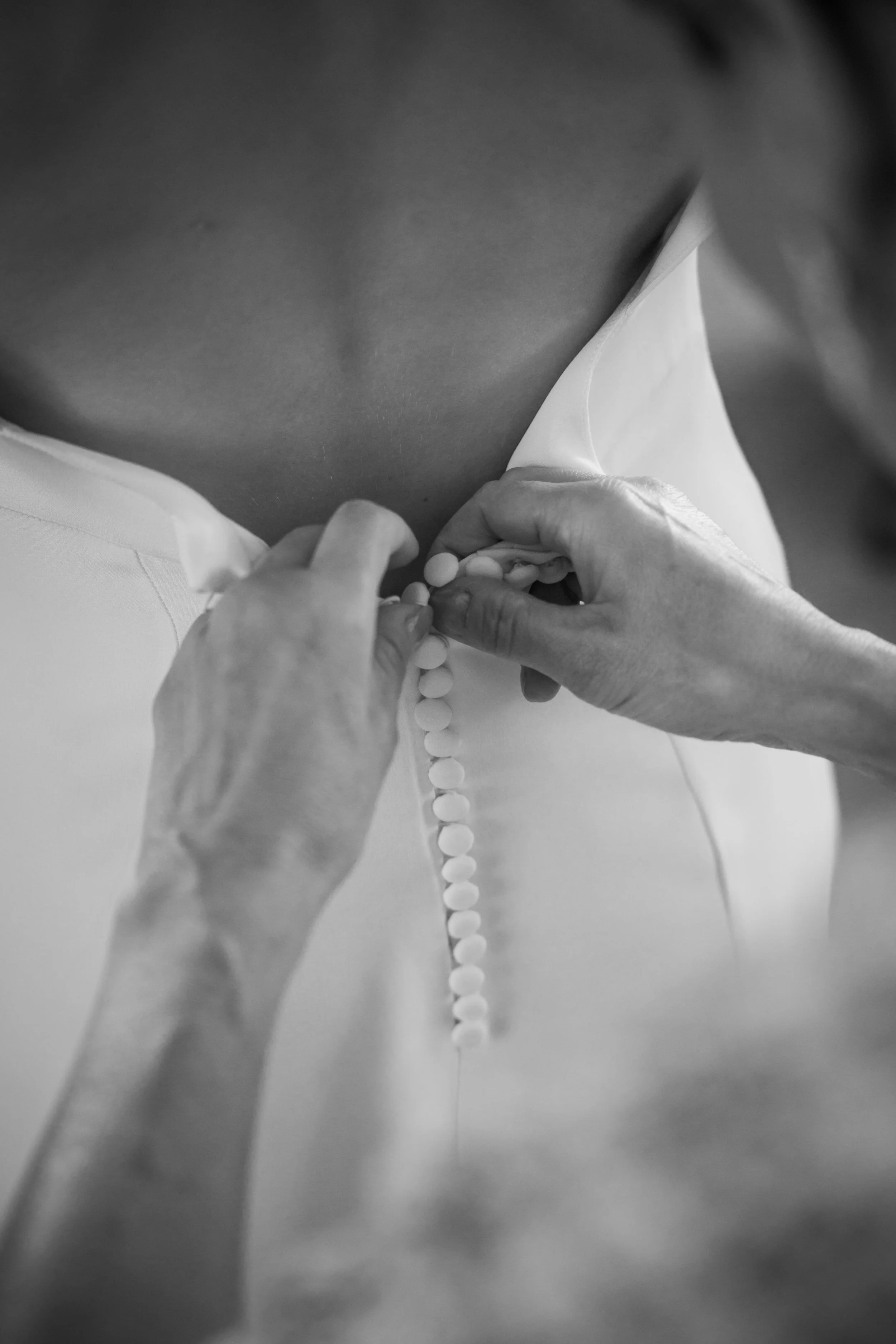 Une personne ferme la boutonnière d'une robe blanche.