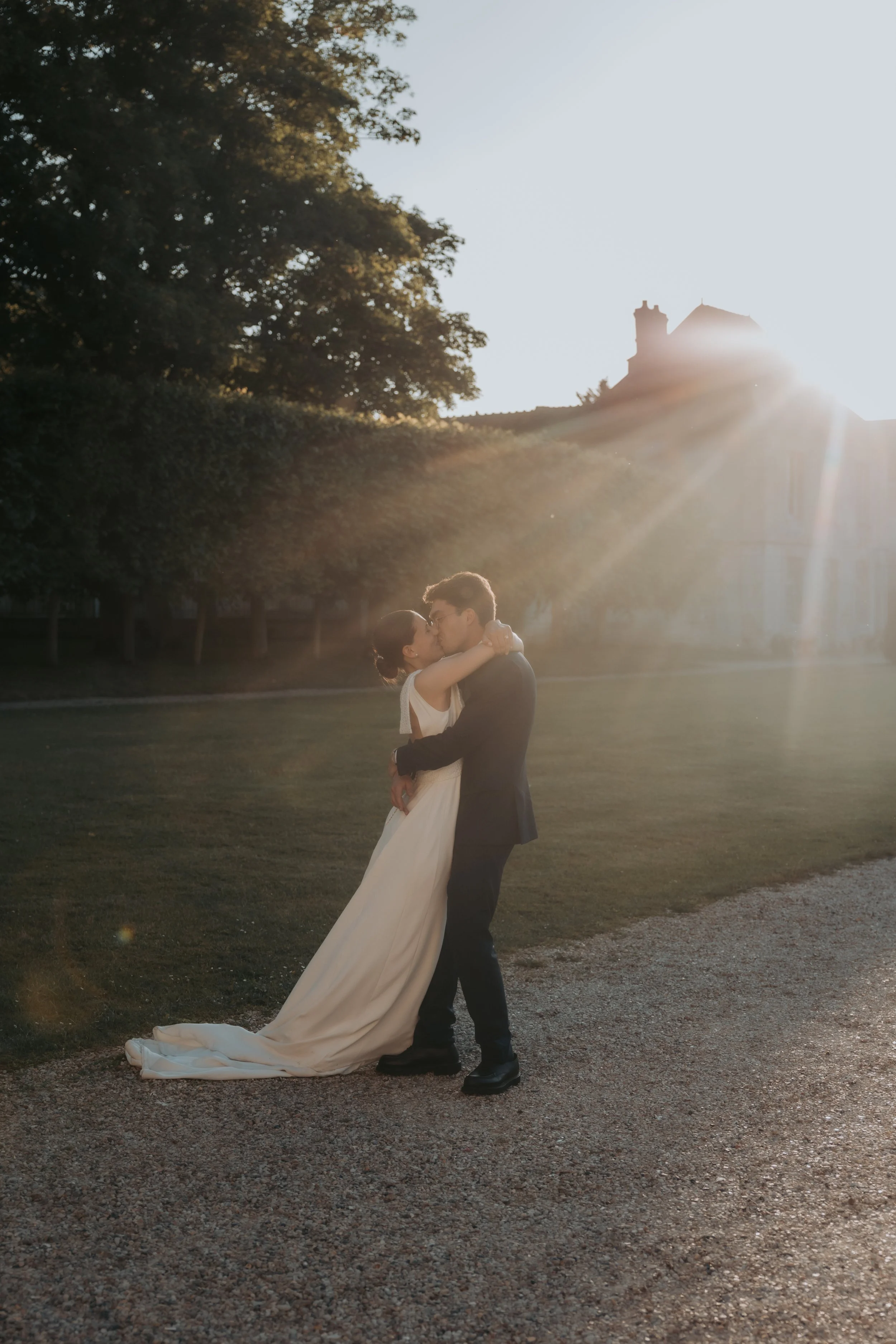 Un couple en robe de mariée et costume s'embrassant dans un parc lors du coucher du soleil. Photo réalisée par Jennifer Buckle photographe de mariage à Paris