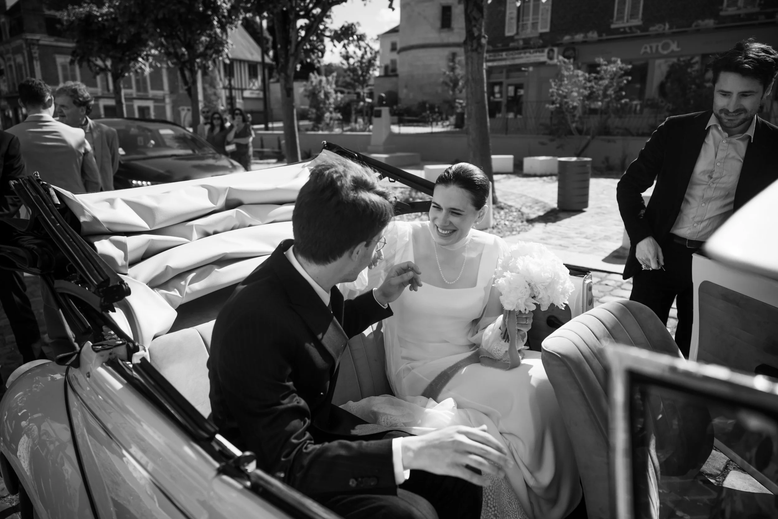 Un couple de mariés souriant dans une calèche, entouré de quelques personnes lors d'une cérémonie en plein air.