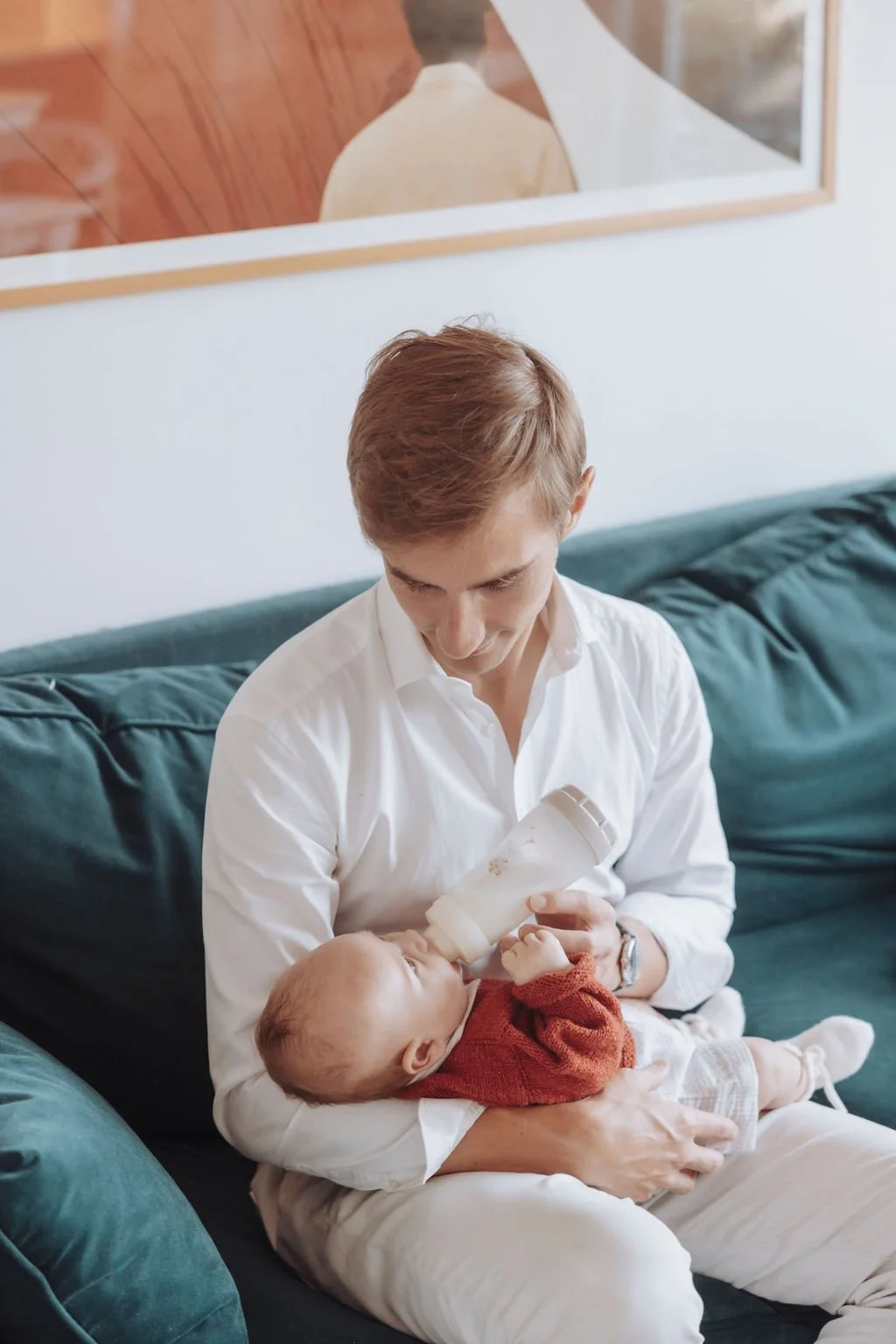Un homme assis sur un canapé nourrit un bébé au biberon.