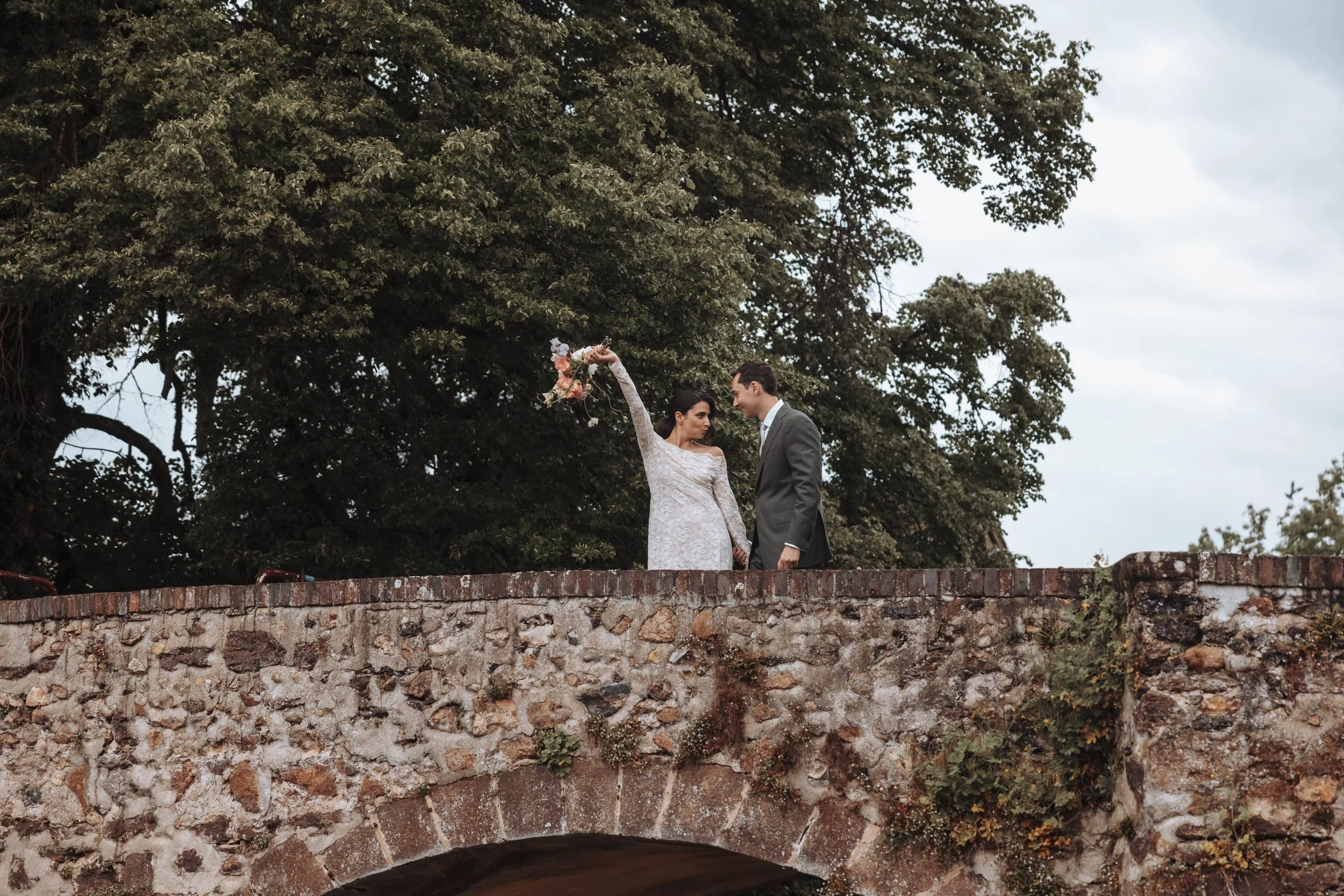 Un couple en tenue de mariage sur un pont en pierre avec des arbres en arrière-plan.