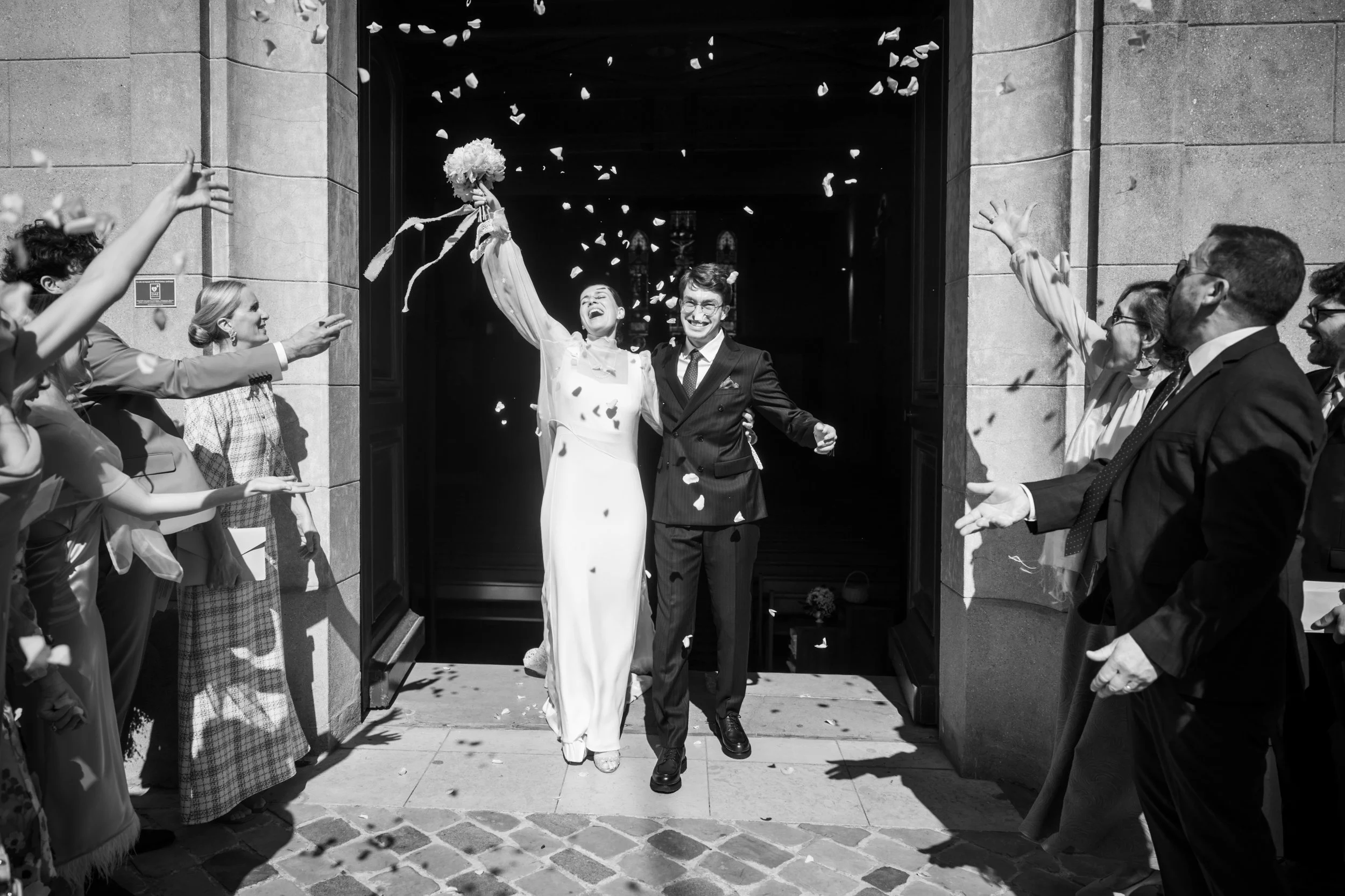 Une mariée et un marié sortant d'une église en jetant des pétales de fleurs, entourés de famille et amis lors d'un mariage à paris . Photo réalisée par Jennifer Buckle photographe de mariage à Paris
