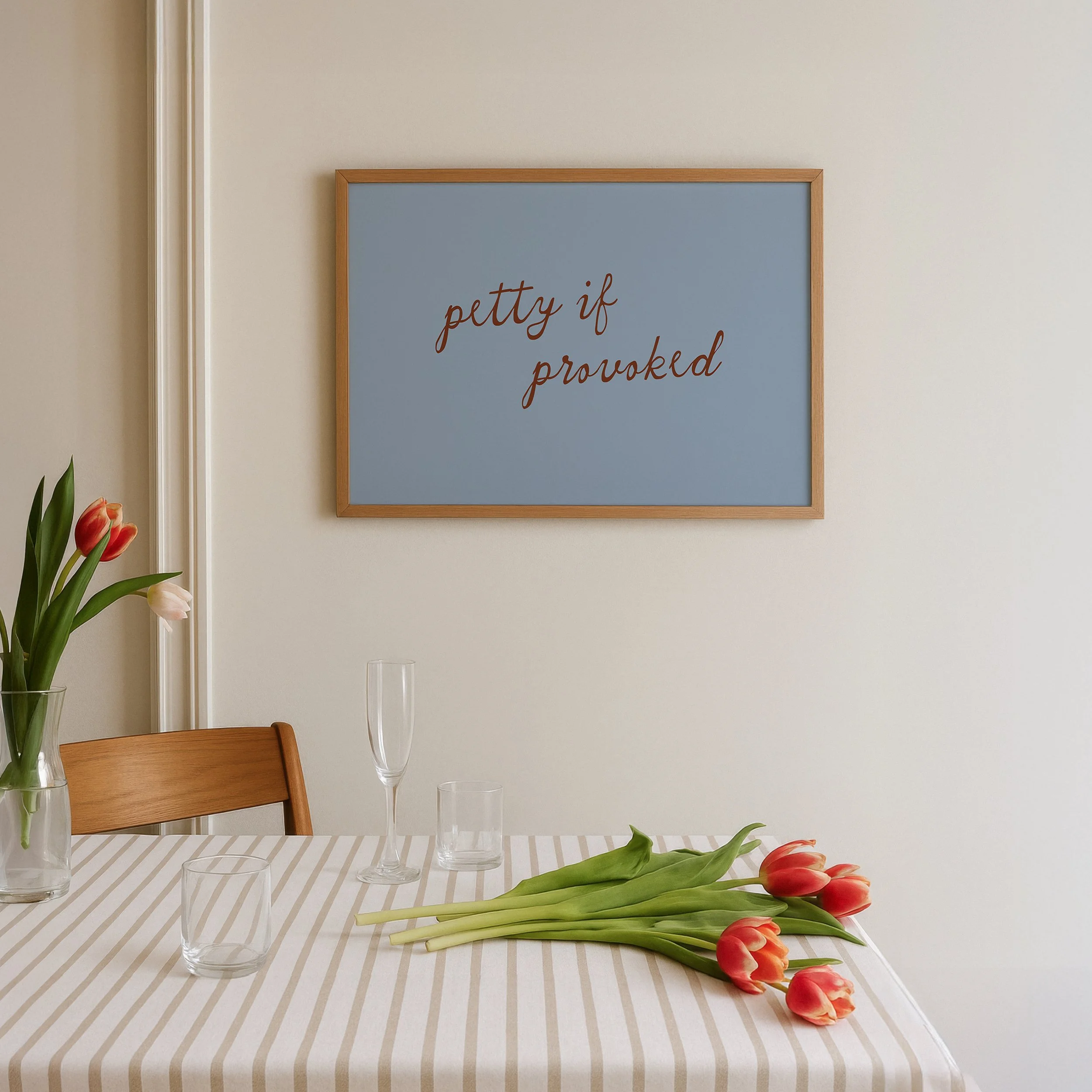 petty if provoked print in blue with red handwritten typography, framed above a striped table with tulips, modern kitchen wall art, funny quote print