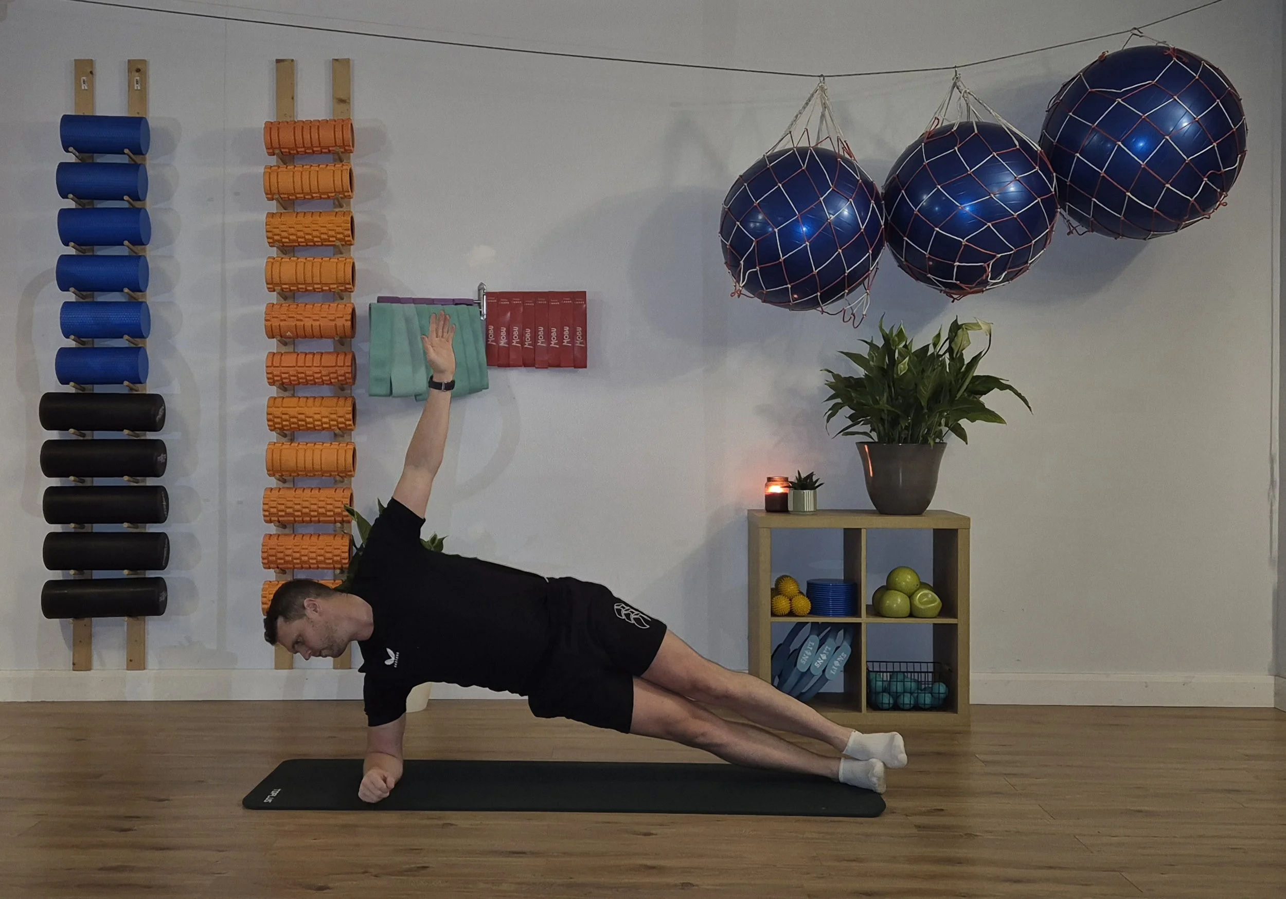 People practicing Pilates on mats in a sunlit studio, sitting and stretching in a seated forward bend pose.
