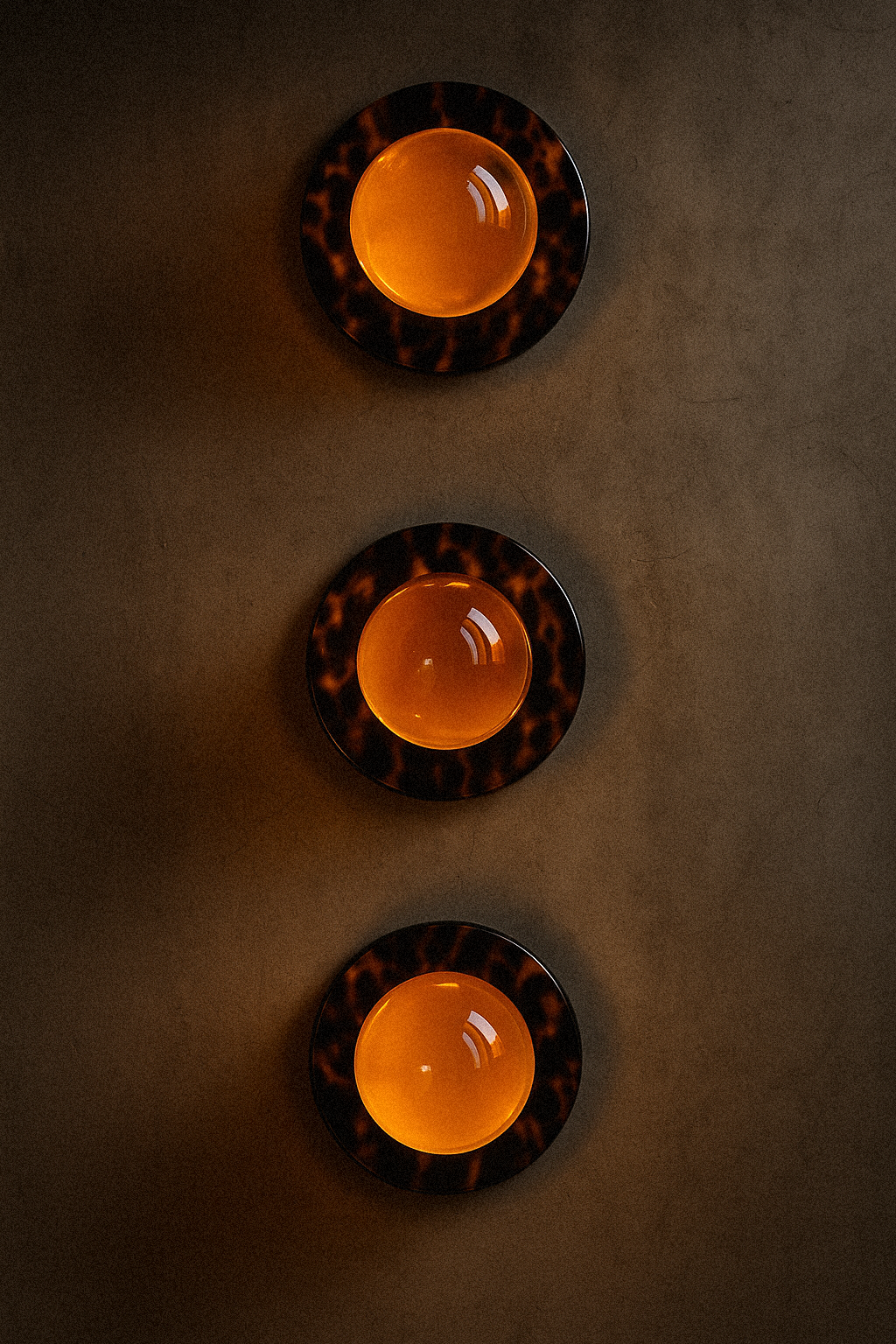 Three round orange lights with black and brown patterned borders are mounted on a dark wall, arranged vertically.