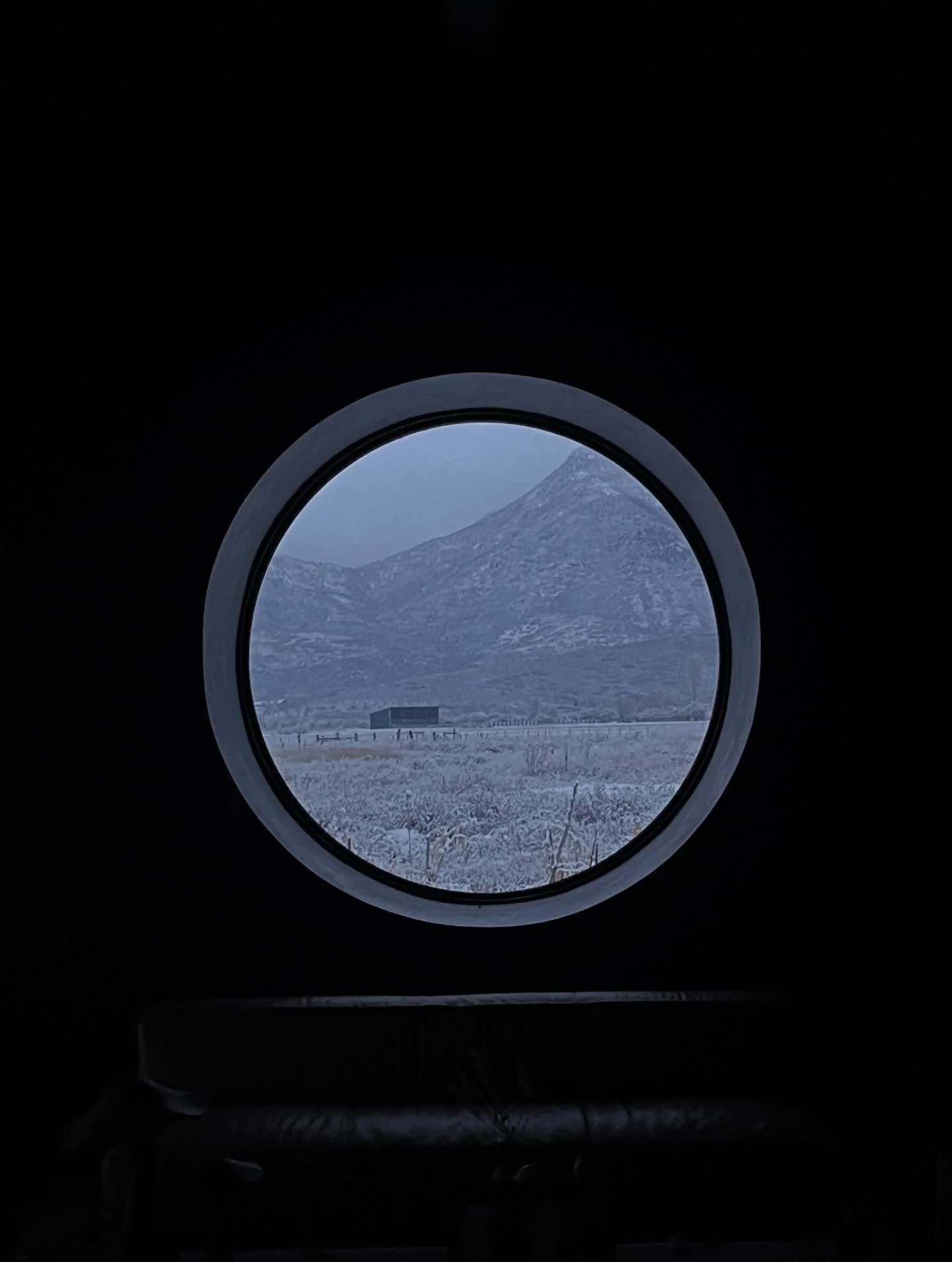 Snow-covered mountains seen through a circular window in a dark room.